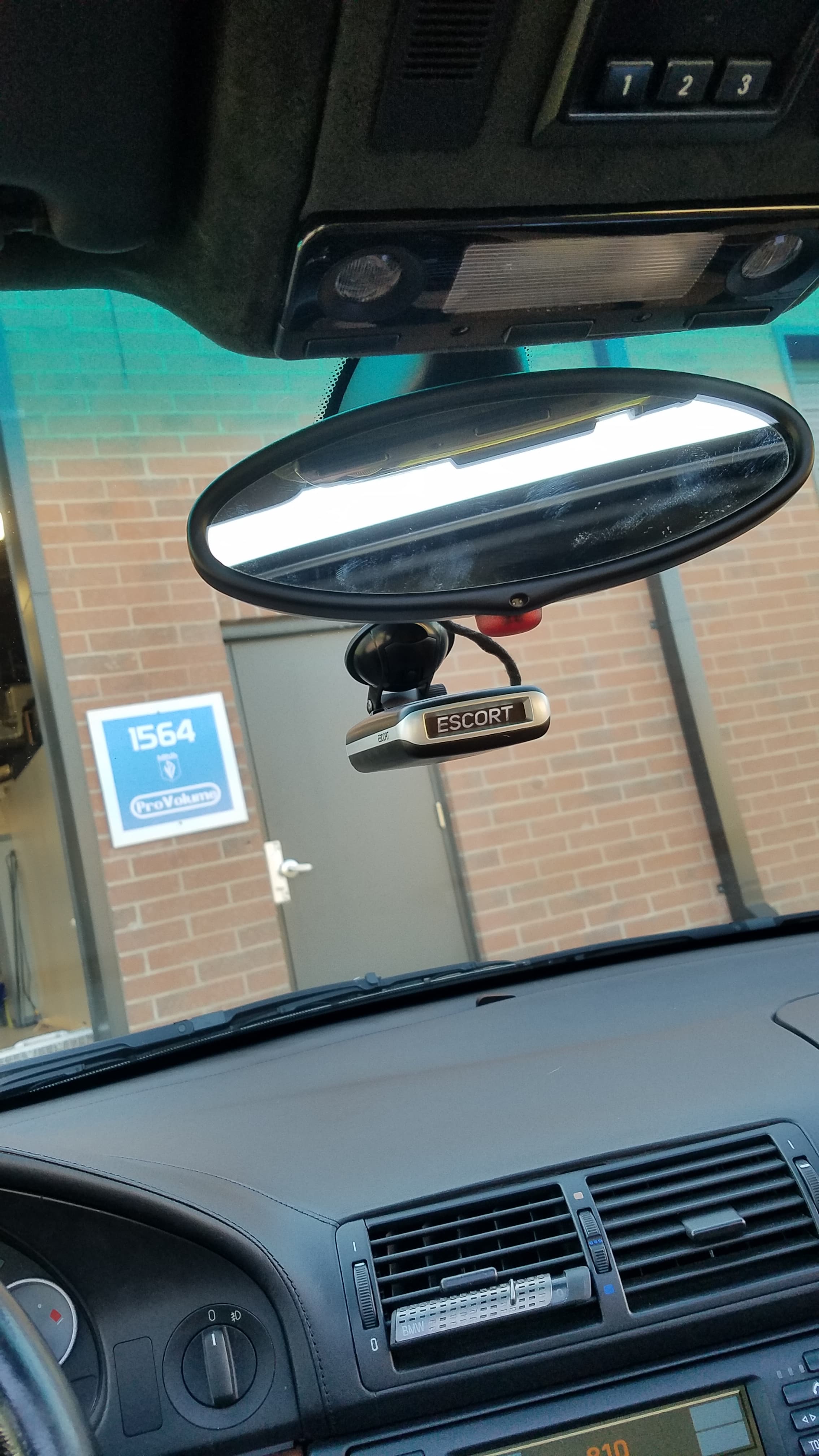Escort radar detector mounted to the windshield of a car below the rearview mirror.