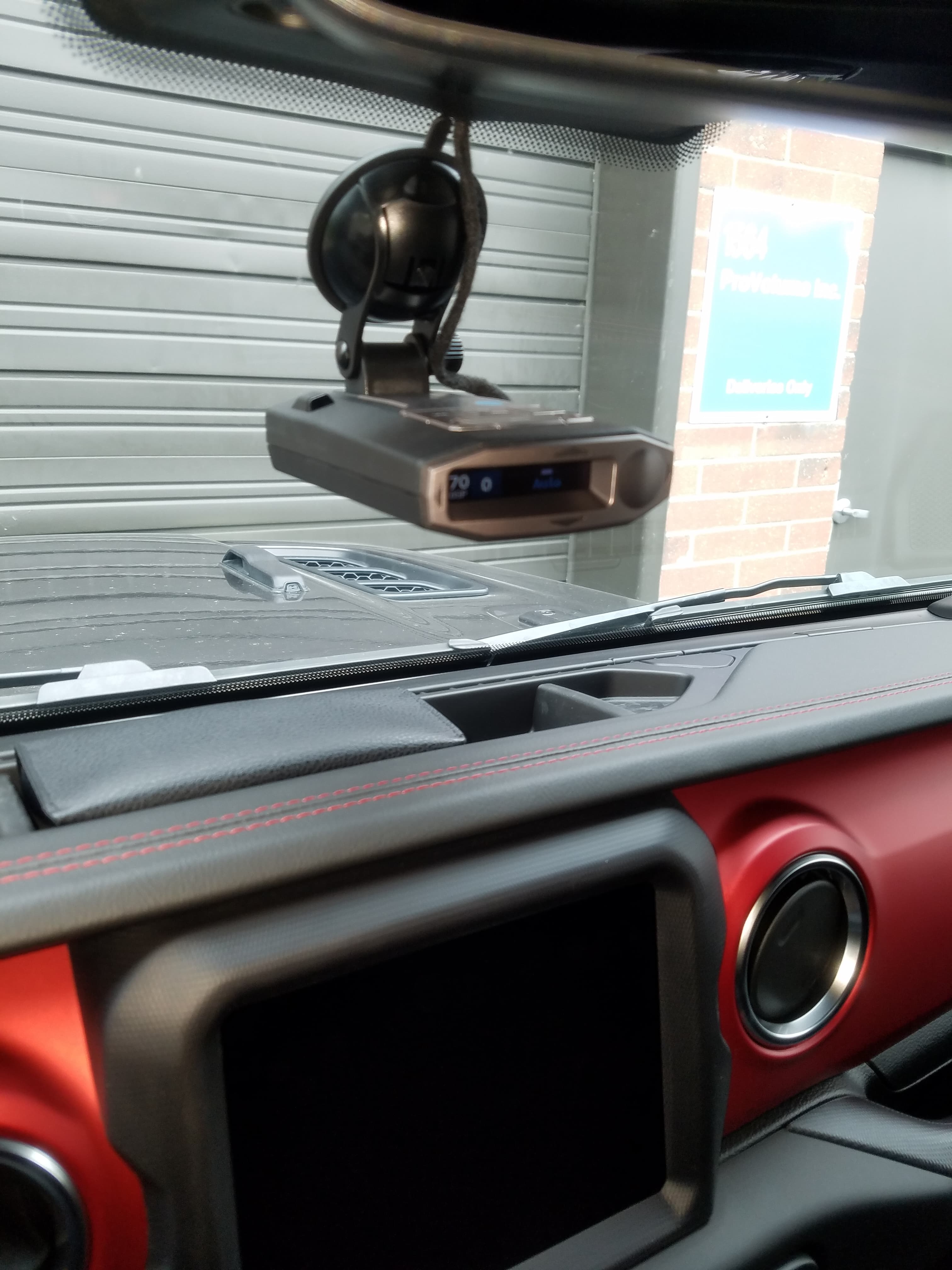 Radar detector mounted on a car windshield above a red and black stitched dashboard.