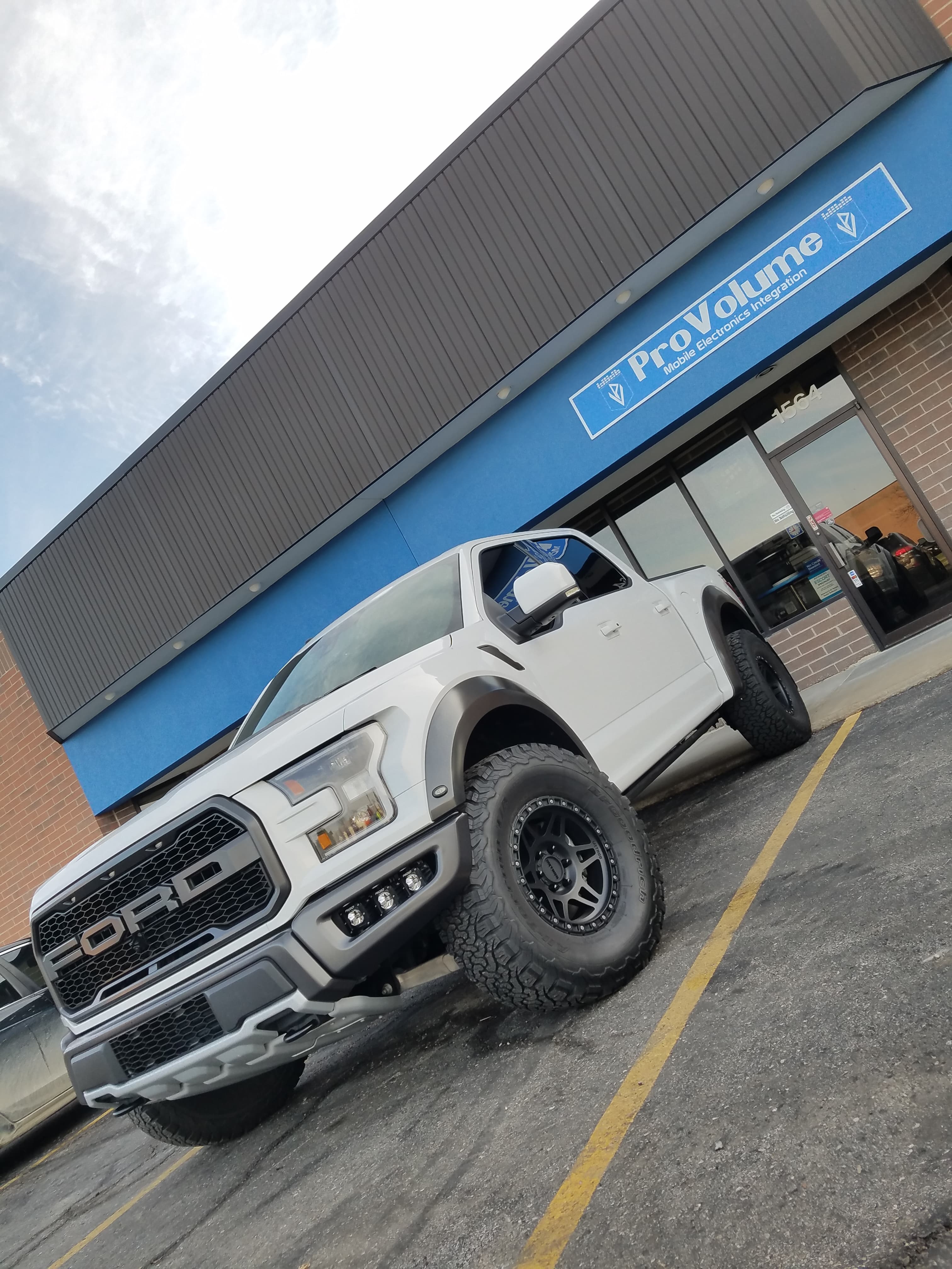 White Ford Raptor with black wheels and off-road tires parked outside a ProVolume store.