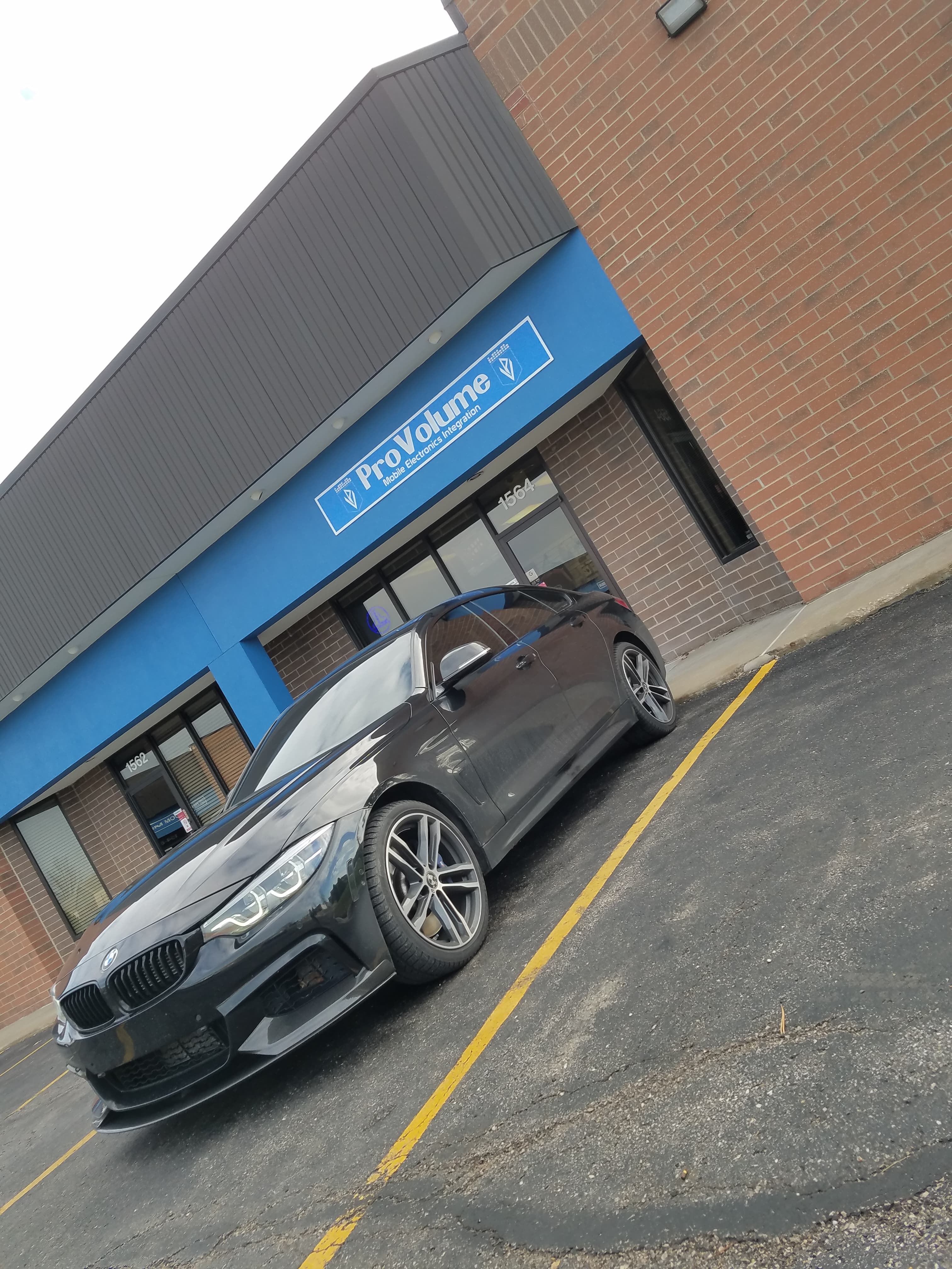 Black BMW sedan parked in front of ProVolume Mobile Electronics Integration with blue signage.