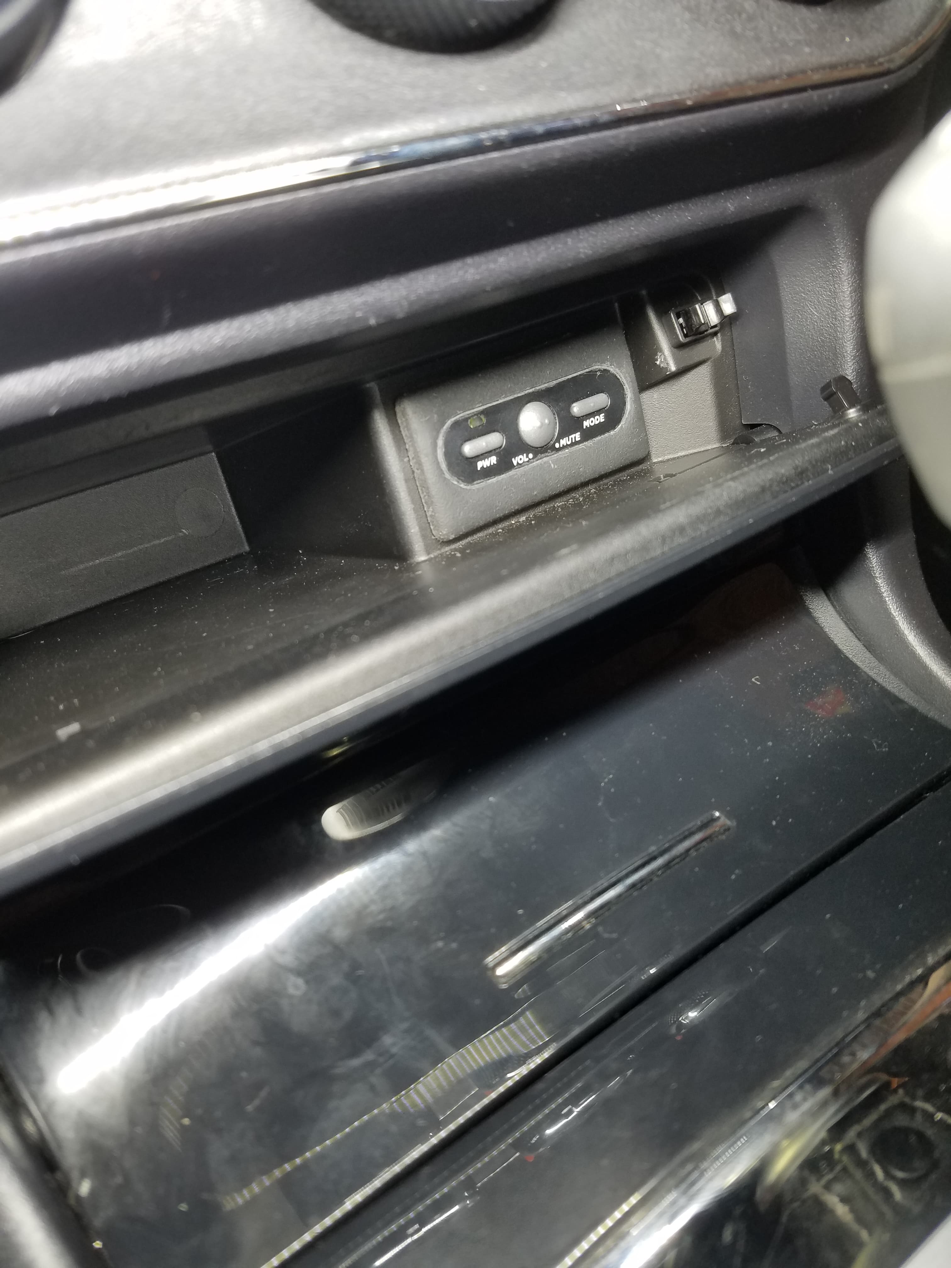 Small control panel with power, volume, mute, and mode buttons inside a car's dashboard compartment.