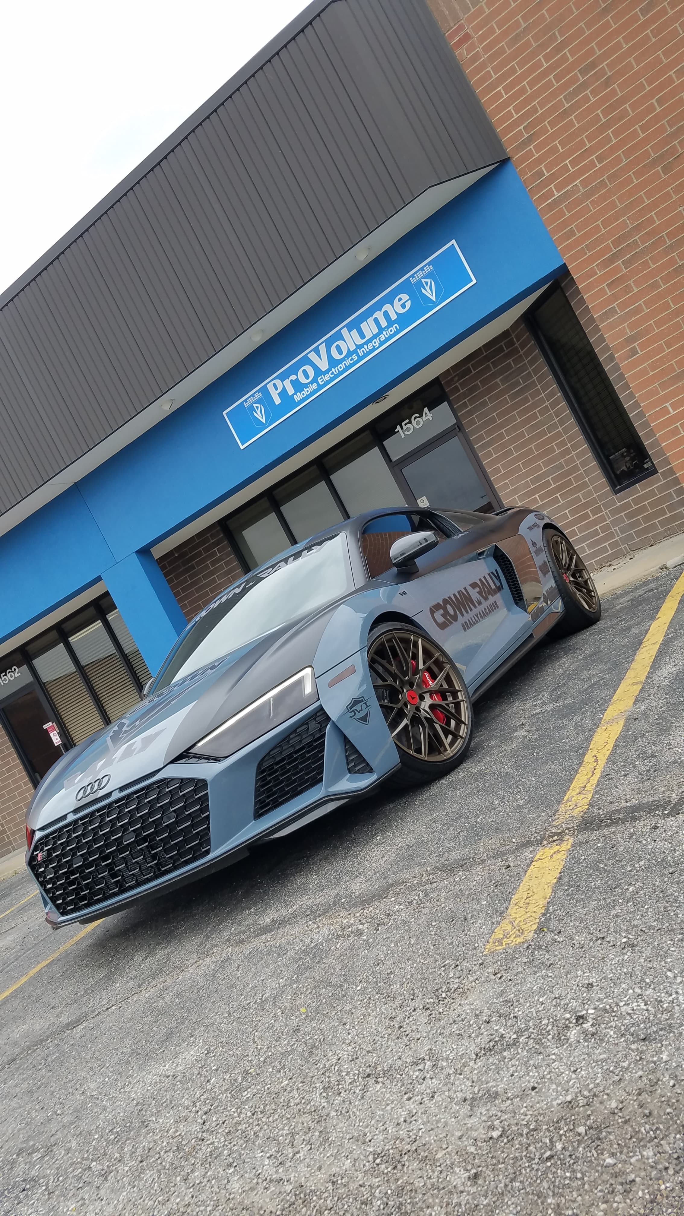 Grey Audi R8 with rally decals parked outside a ProVolume mobile electronics store.