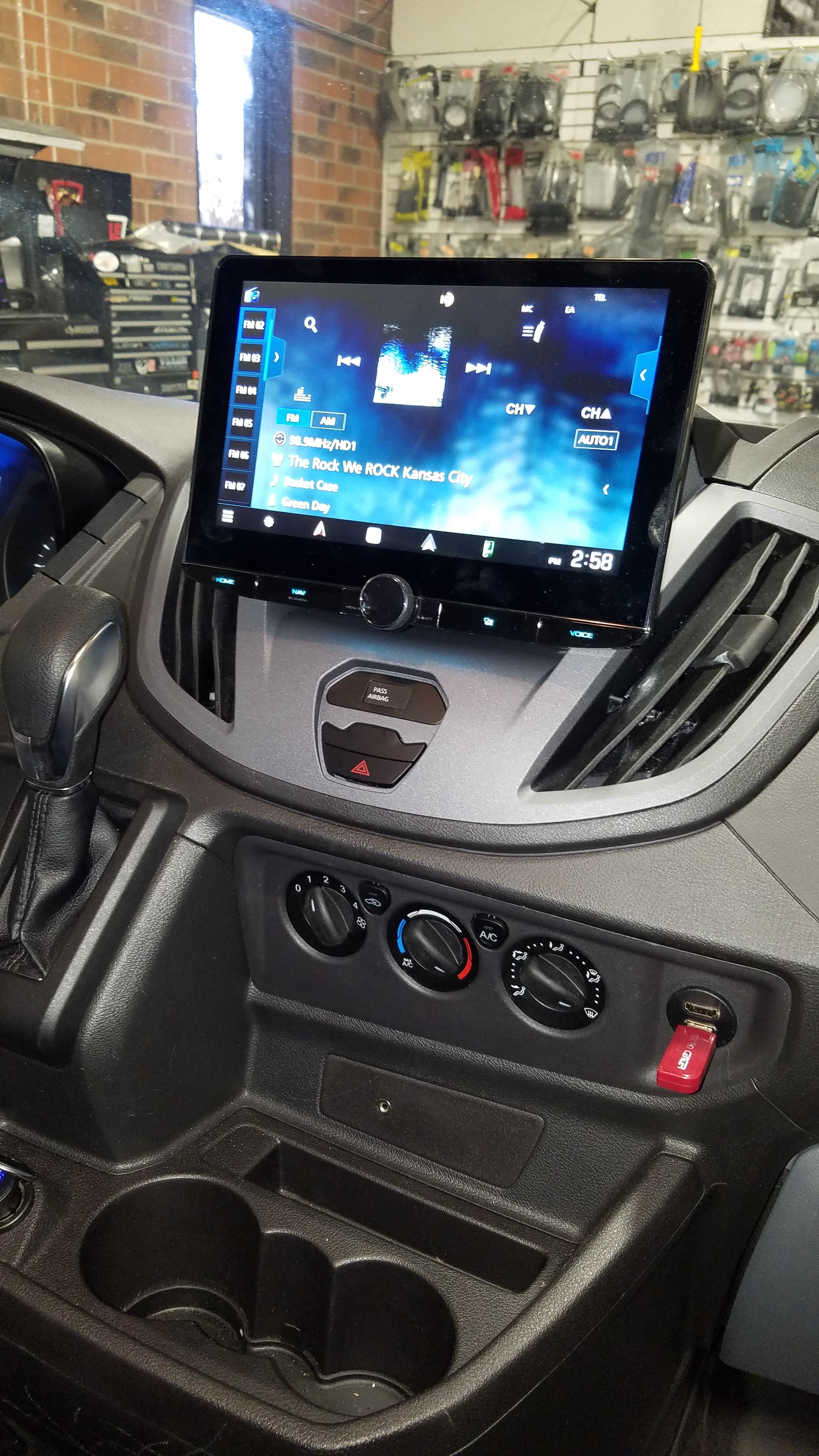 Touchscreen infotainment system installed in a vehicle dashboard above climate controls and a gear shifter.