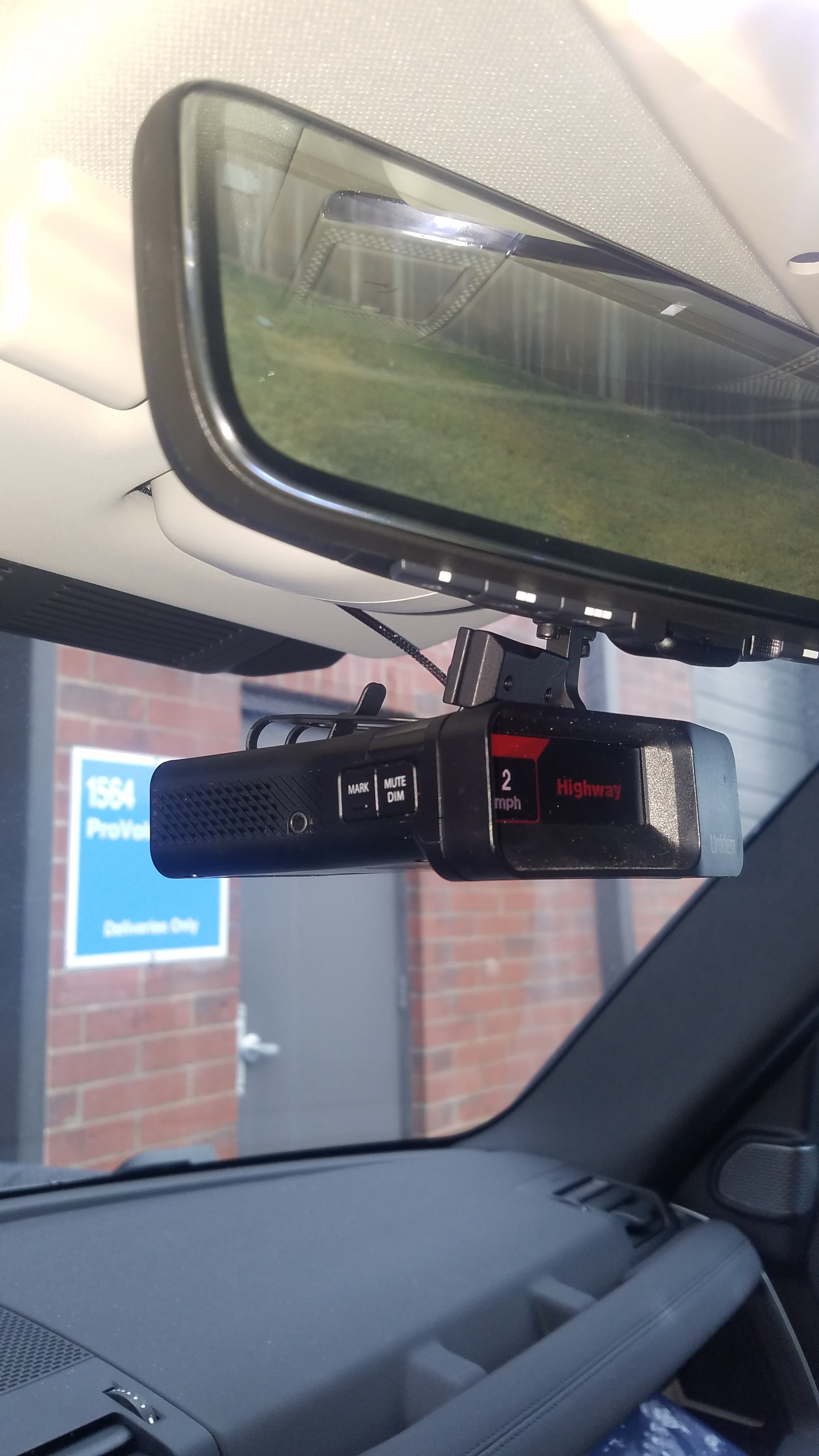 A black Uniden radar detector mounted below a rearview mirror, displaying speed and highway mode.