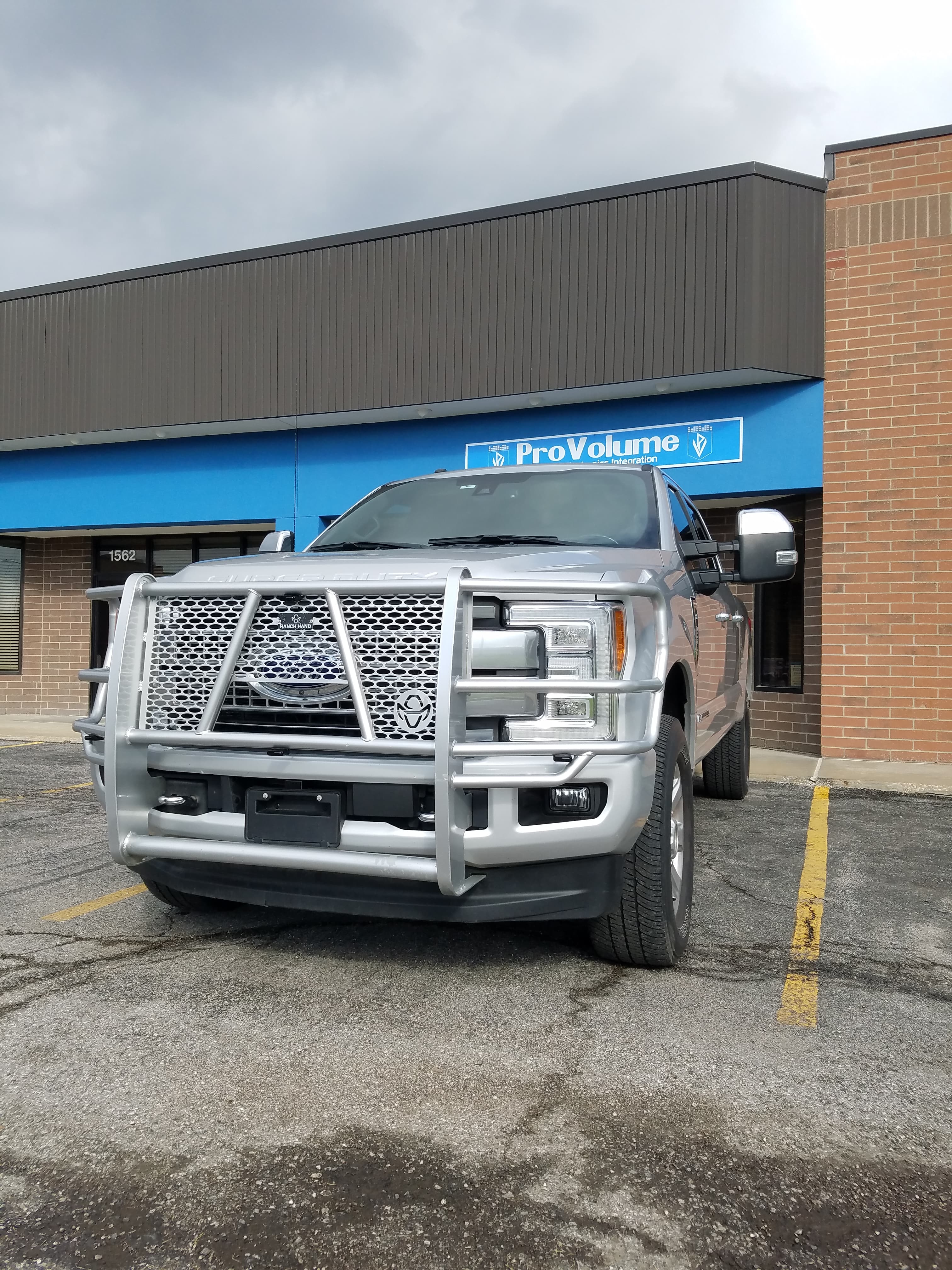Silver Ford Super Duty truck with a large silver brush guard parked outside a storefront.