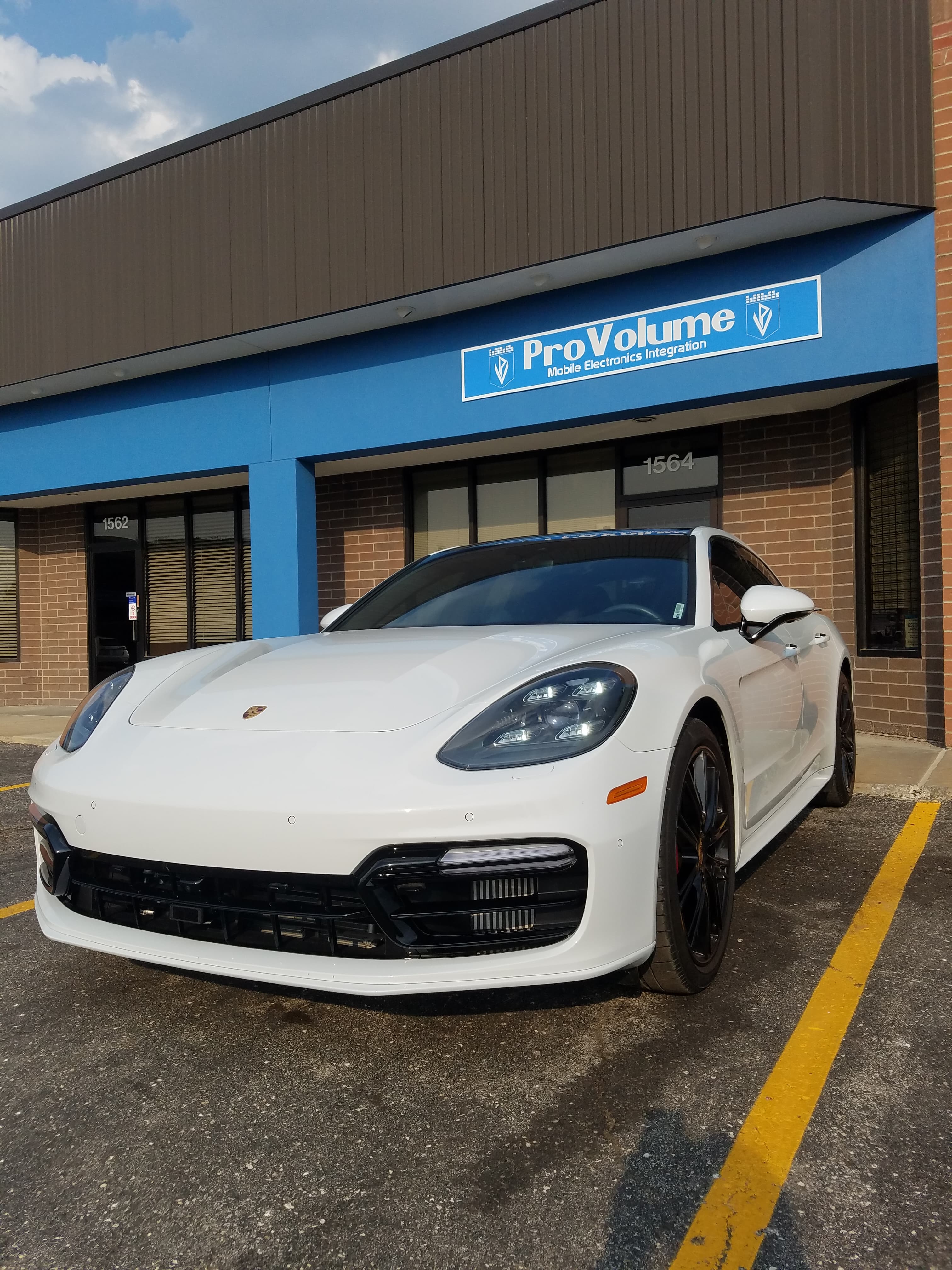 White Porsche Panamera parked in front of a ProVolume Mobile Electronics Integration storefront.
