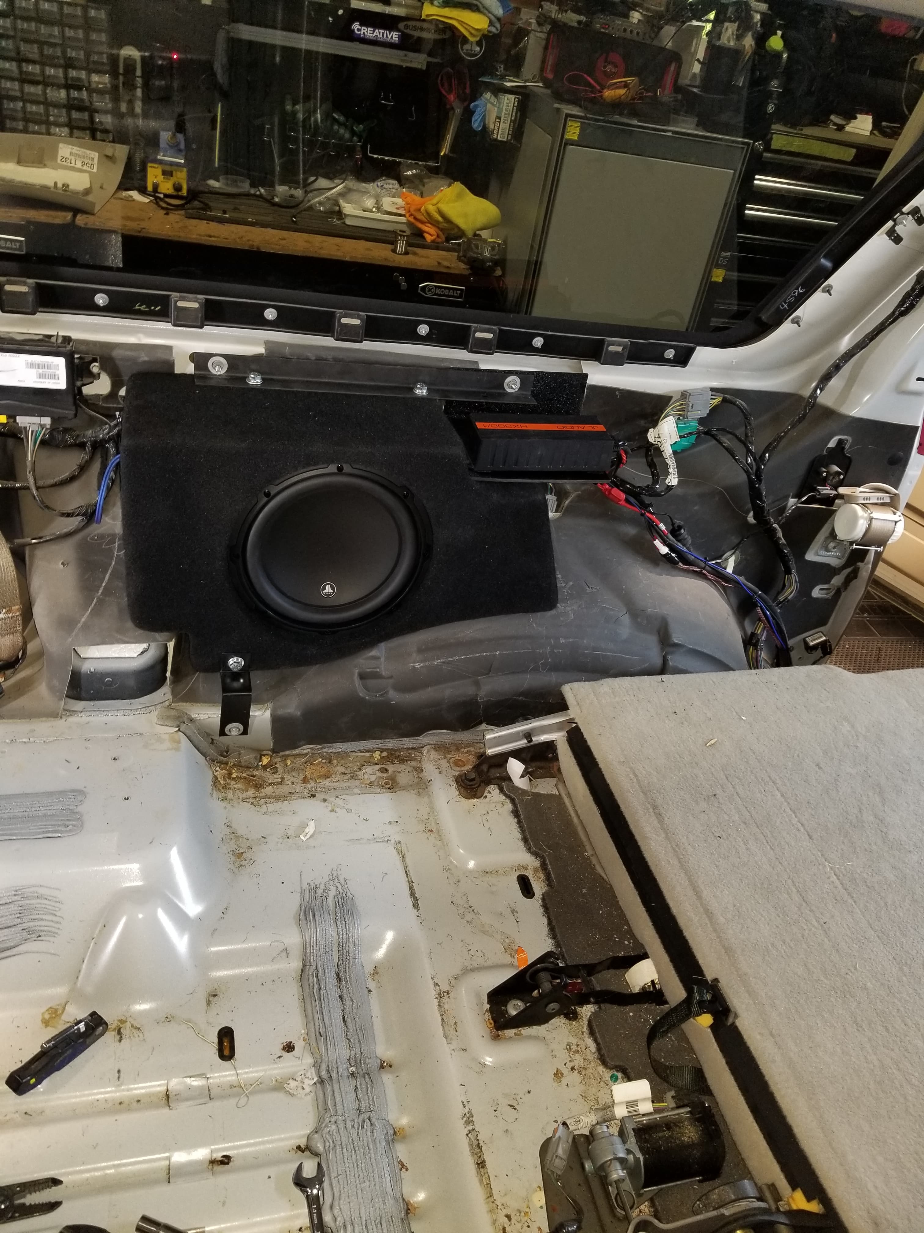 Subwoofer and amplifier mounted in a black enclosure inside a vehicle's rear cargo area.