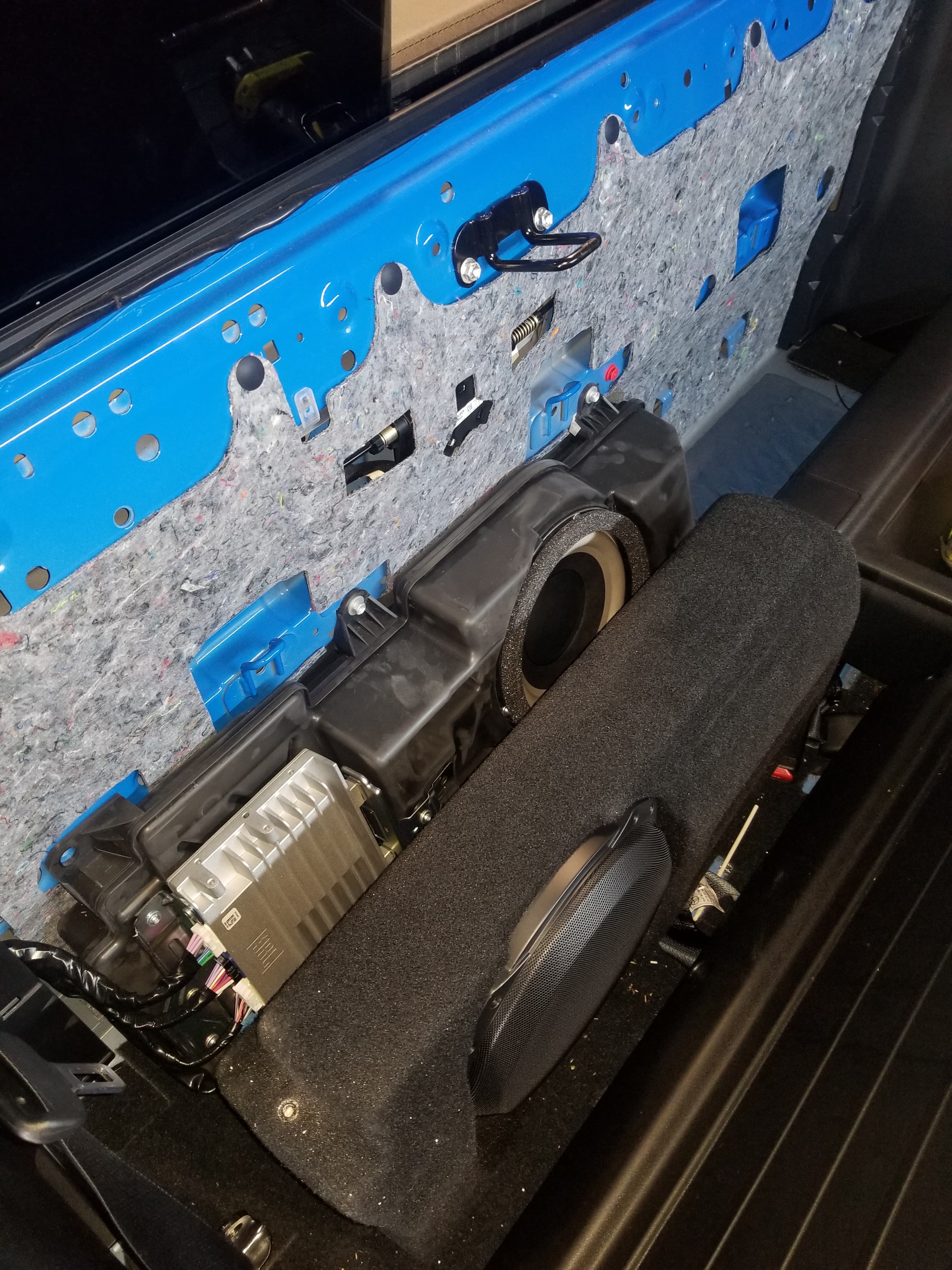 Subwoofer and amplifier assembly mounted against the insulated rear wall of a blue truck.