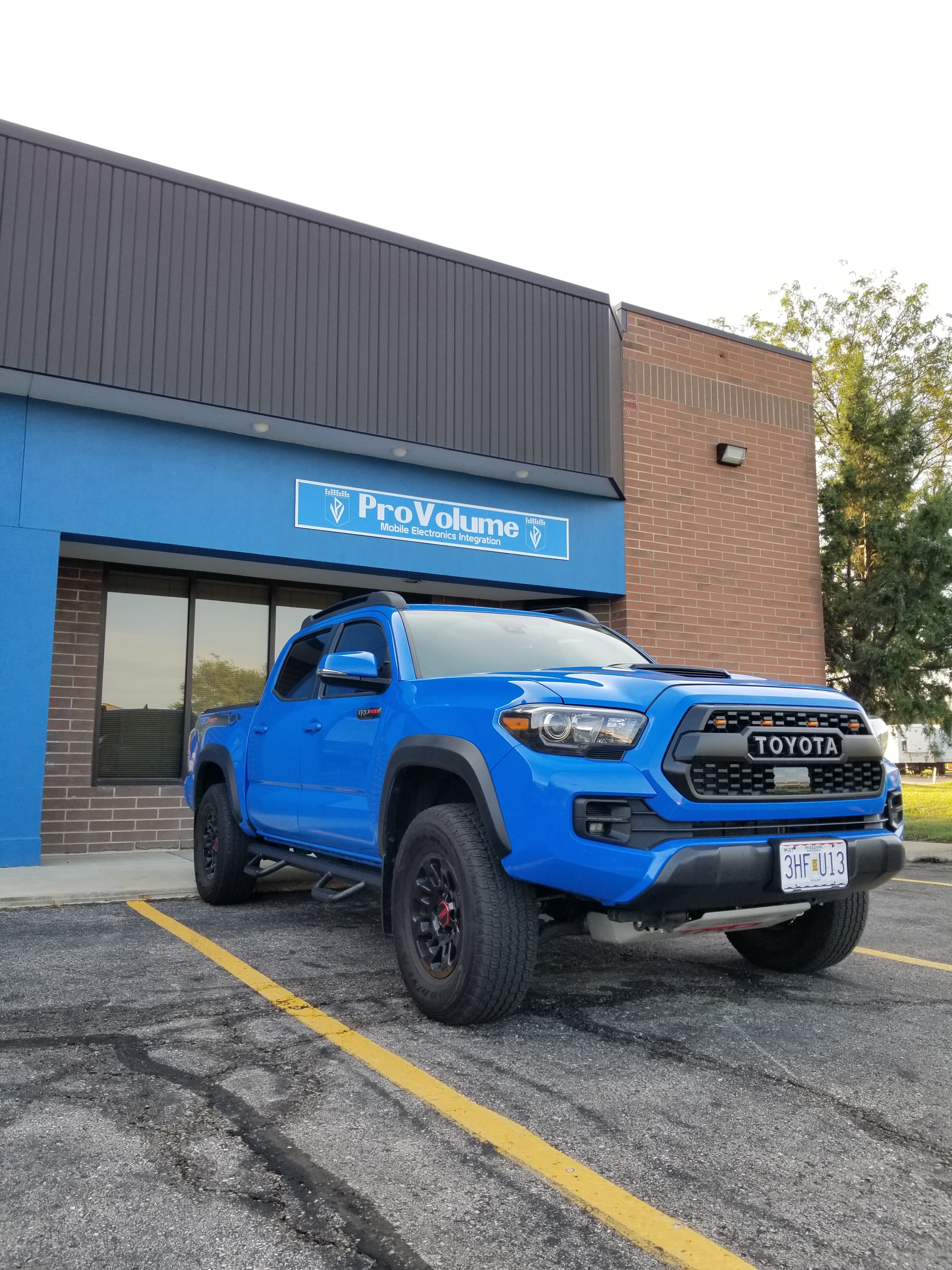 Bright blue Toyota Tacoma TRD Pro parked outside a ProVolume mobile electronics integration store.