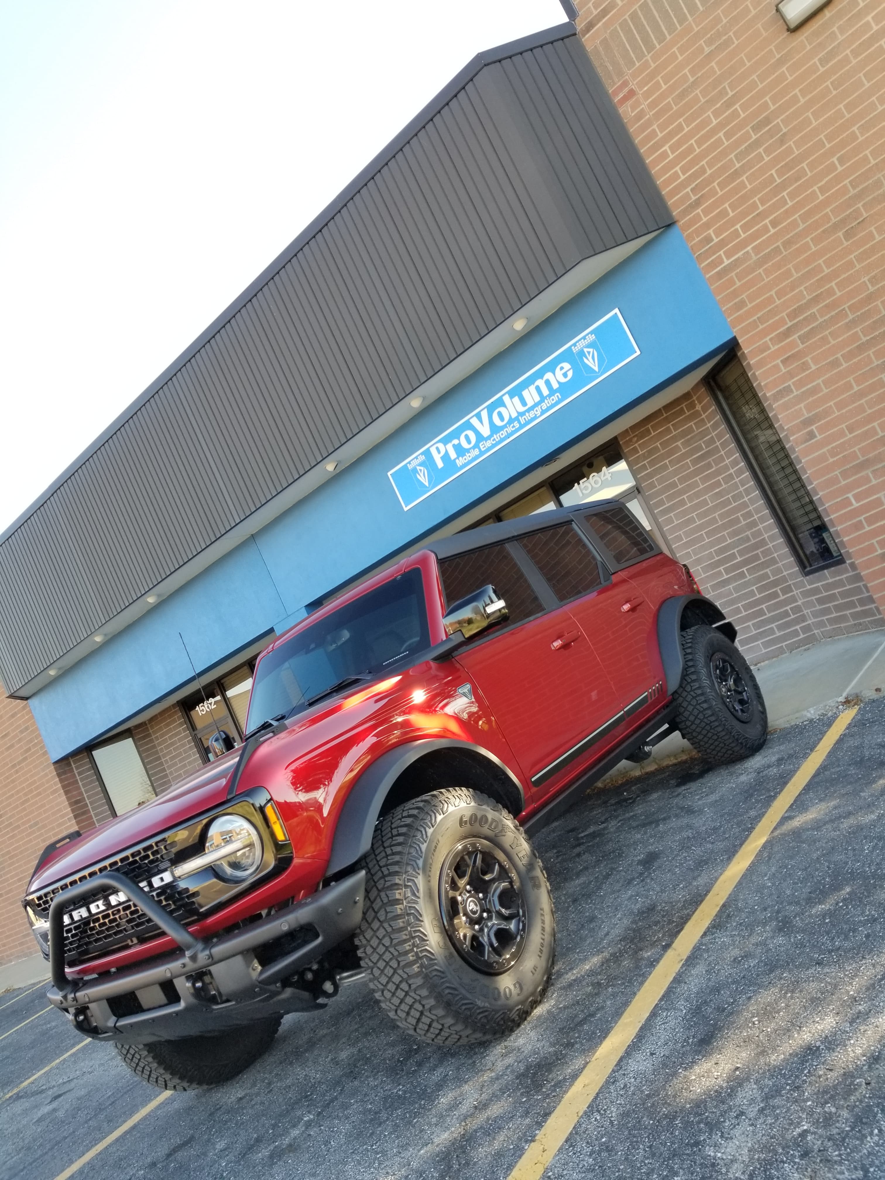Red Ford Bronco with large off-road tires parked outside a ProVolume mobile electronics store.