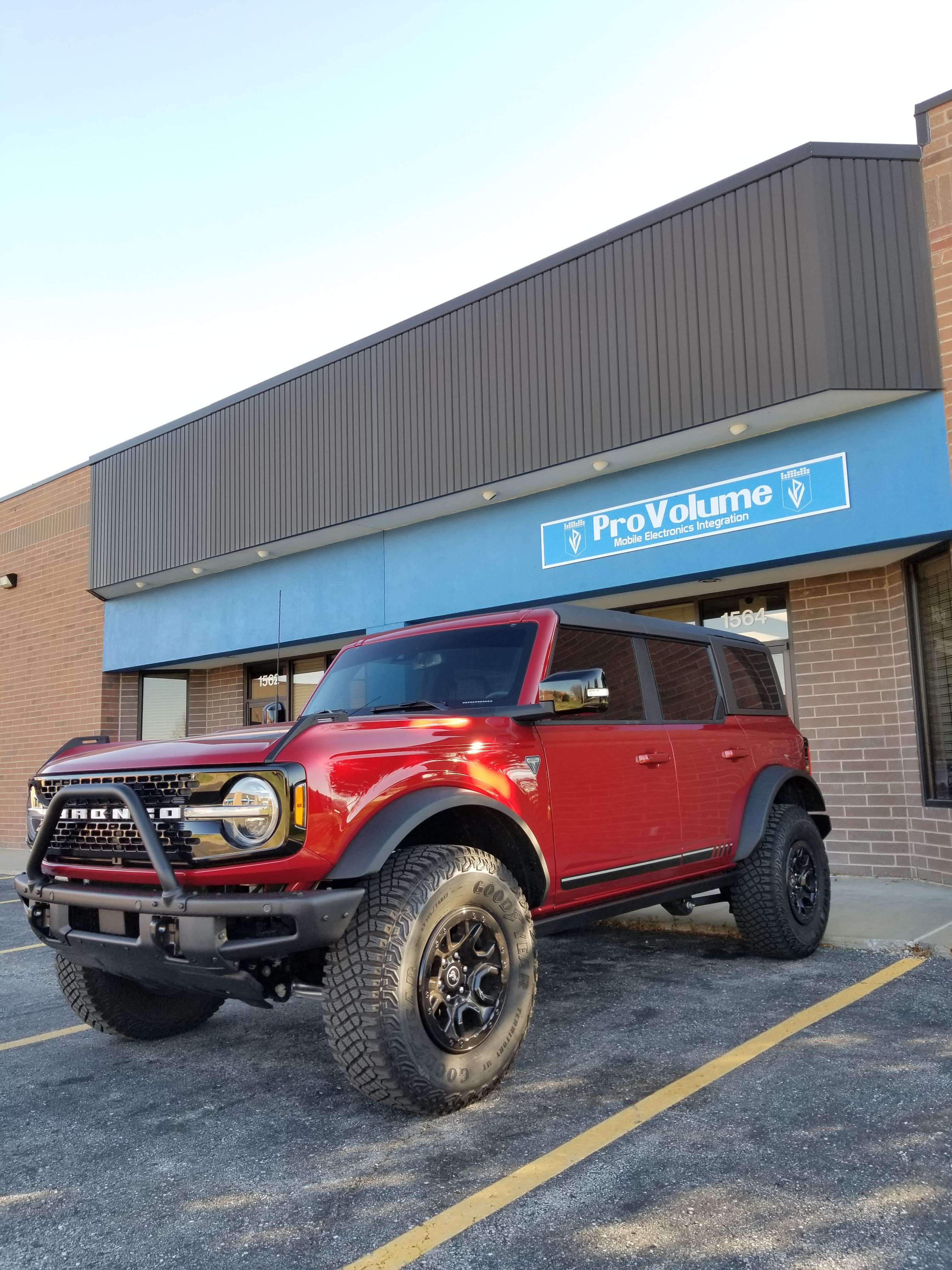 Red Ford Bronco with off-road tires parked in front of a ProVolume electronics store.