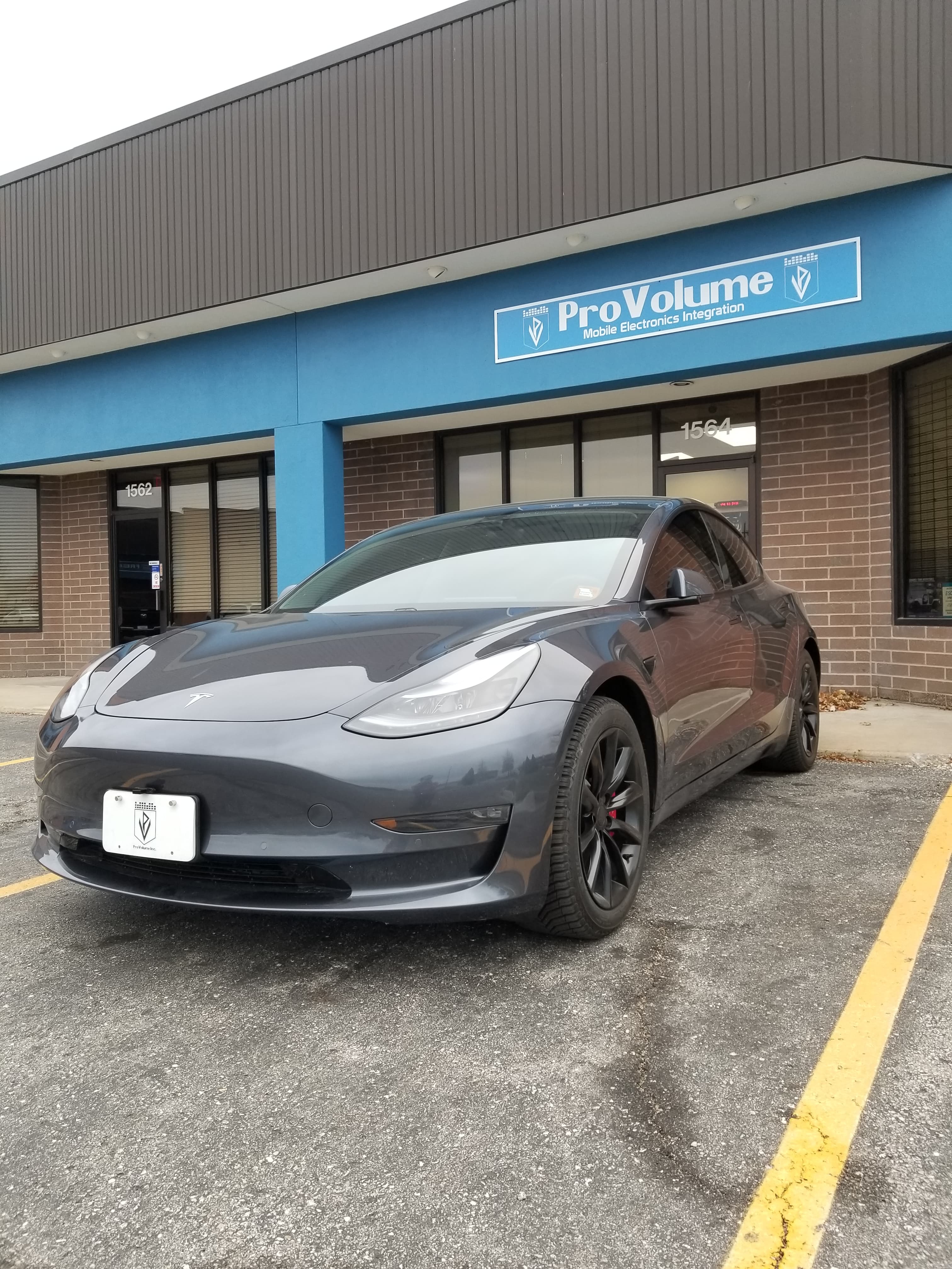 Dark grey Tesla Model 3 parked outside a ProVolume Mobile Electronics Integration shop.