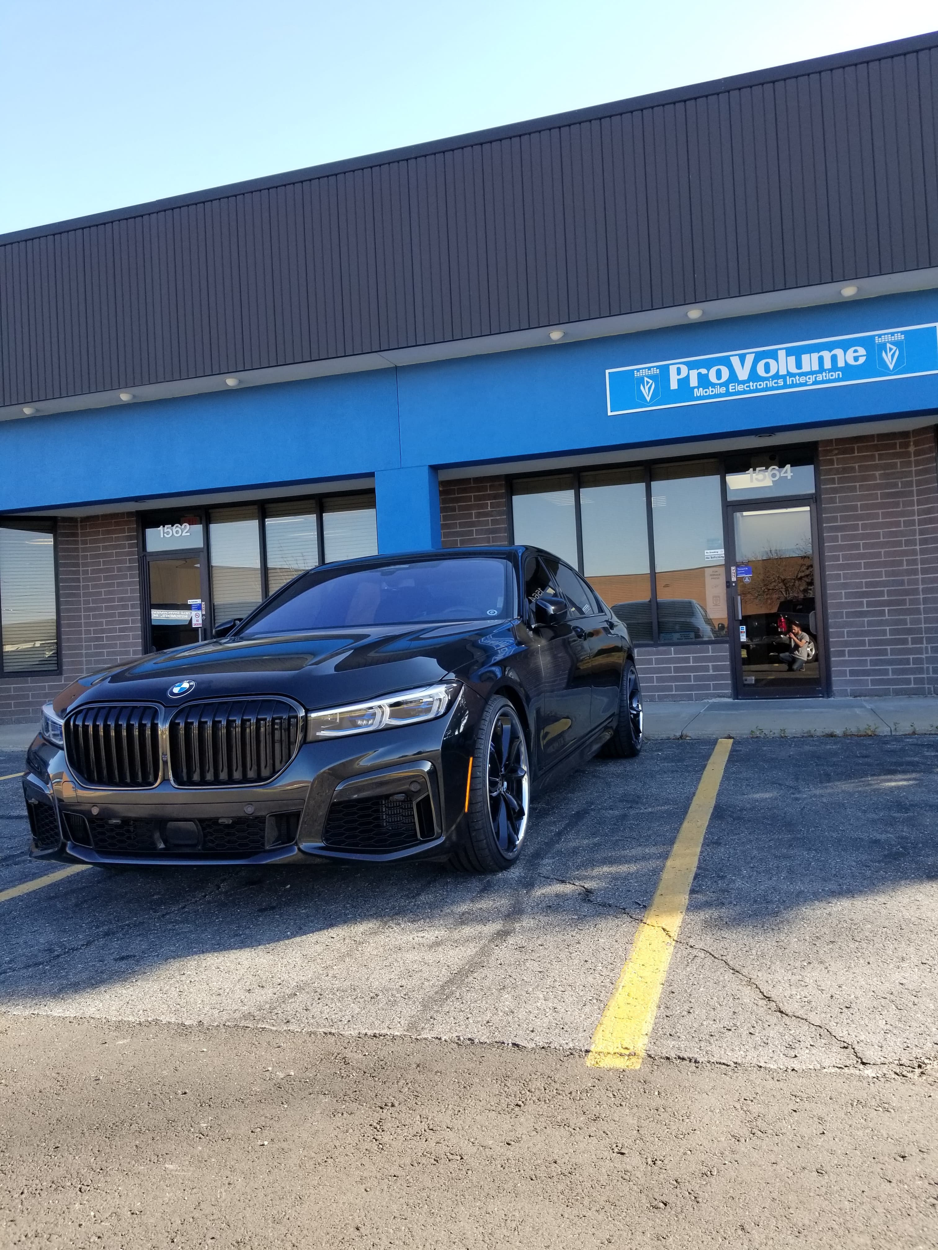 Black BMW sedan parked in front of a blue ProVolume mobile electronics integration business.