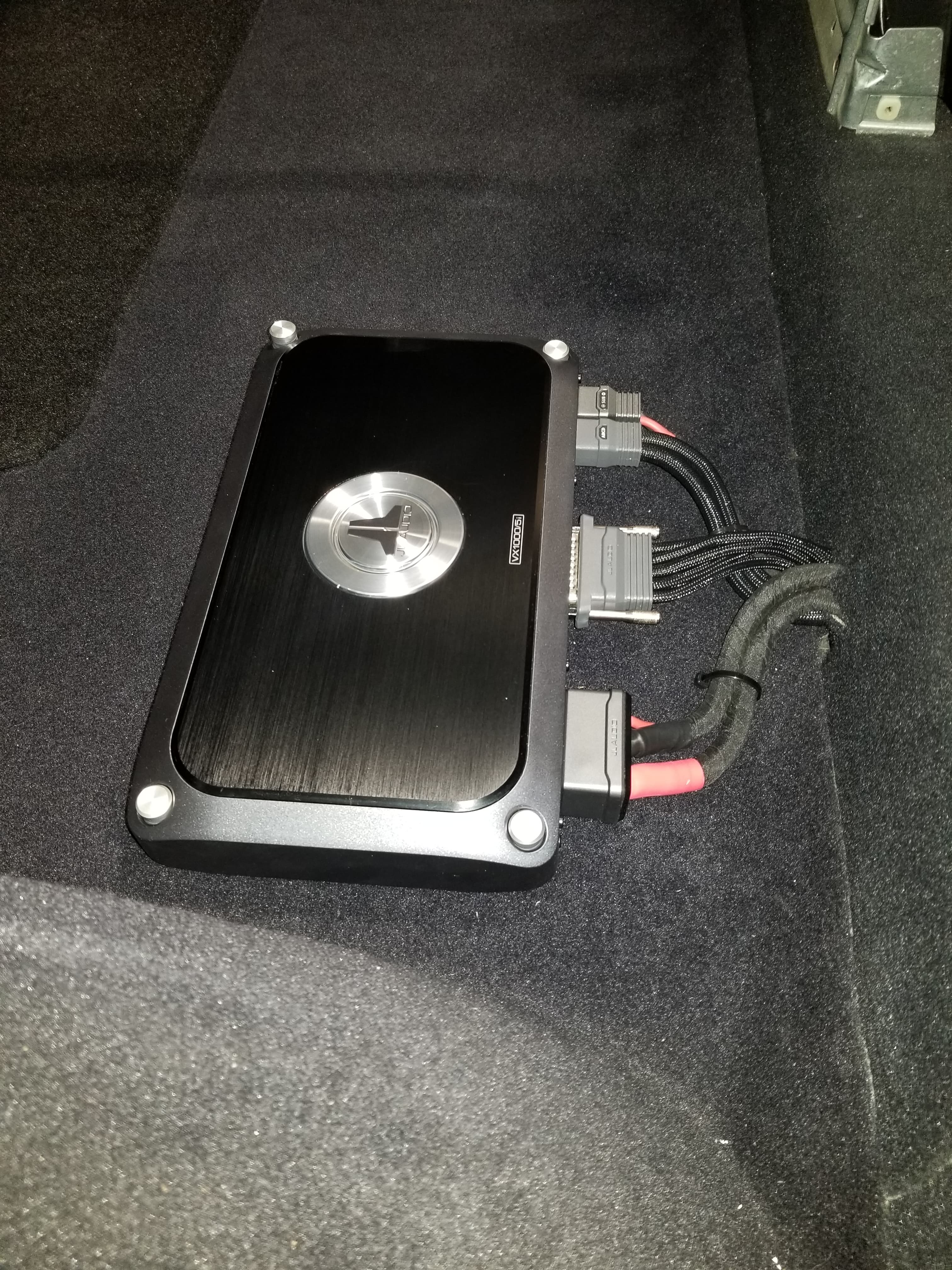 Black JL Audio VX1000/5i car amplifier with bundled wiring installed on dark carpet.