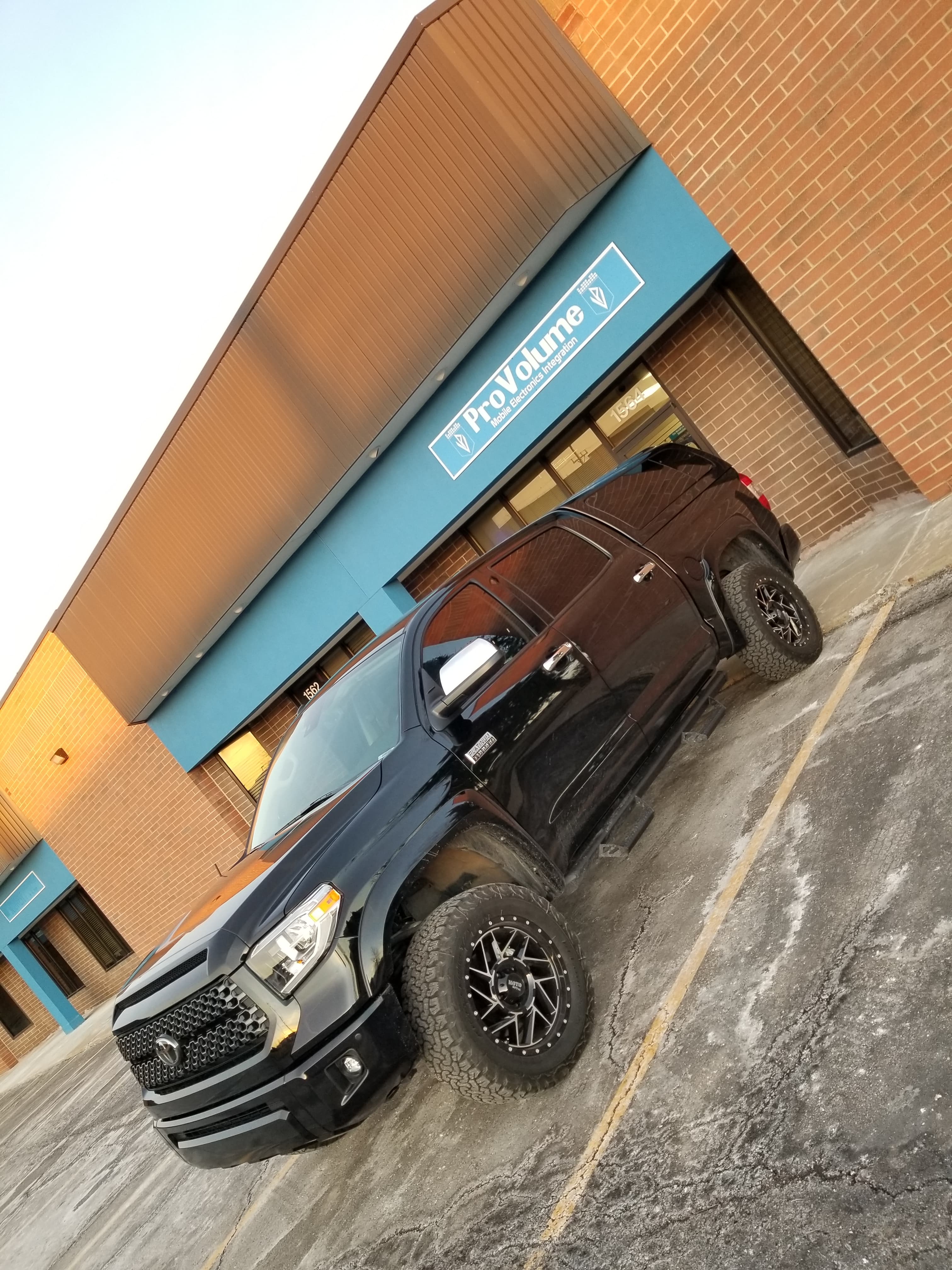 Lifted black Toyota Tundra pickup truck parked in front of a ProVolume electronics store.
