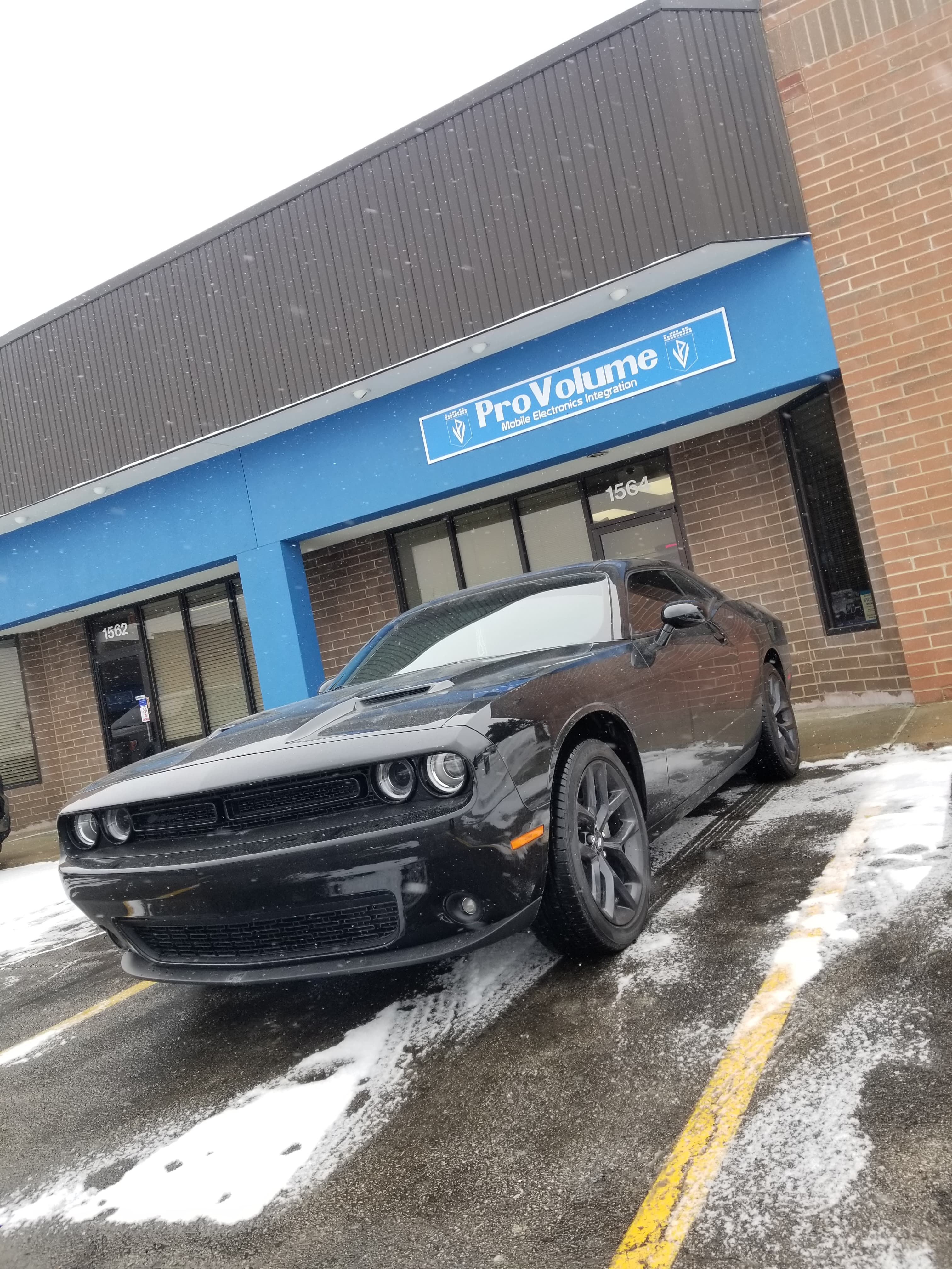 Black Dodge Challenger parked in front of a ProVolume electronics store in the snow.