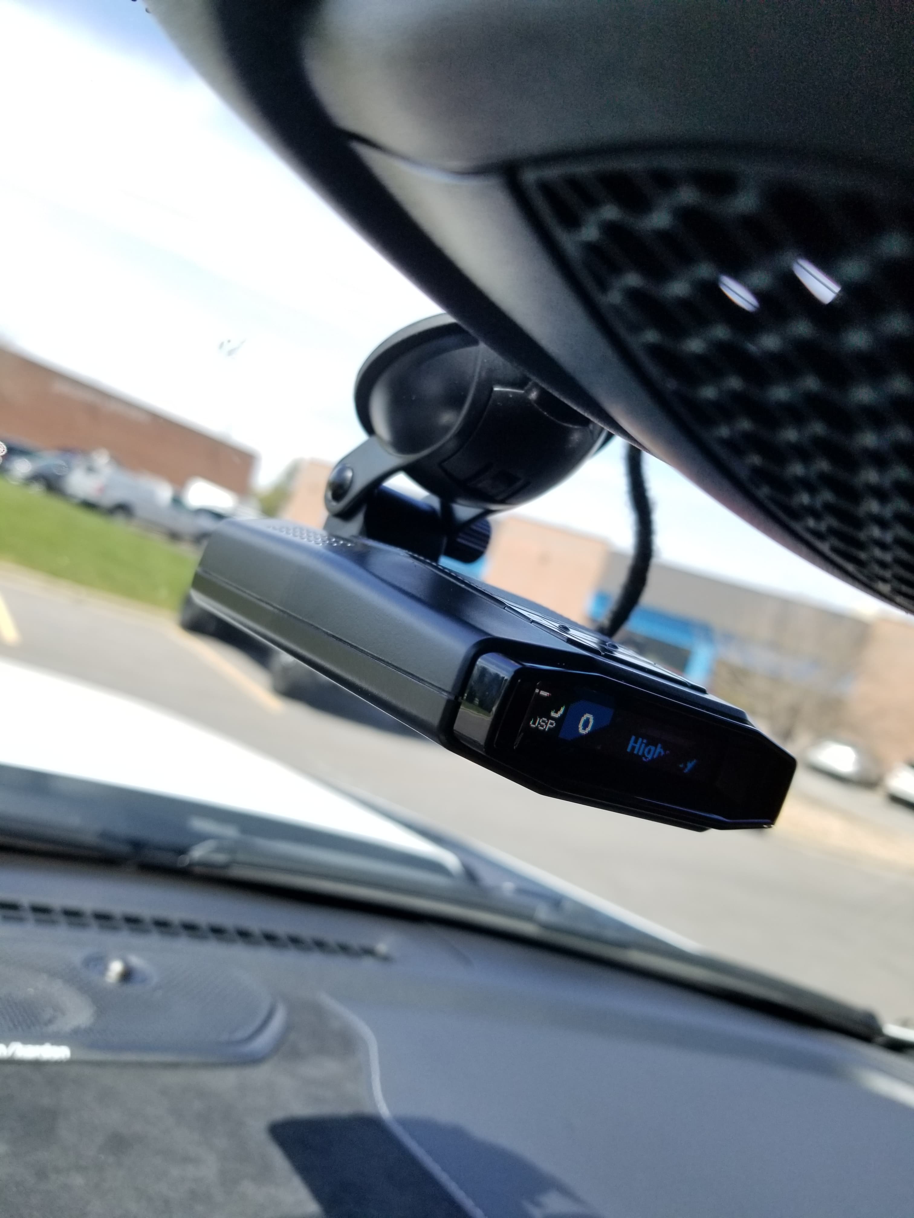 Black radar detector mounted on a car windshield with a suction cup and digital display.