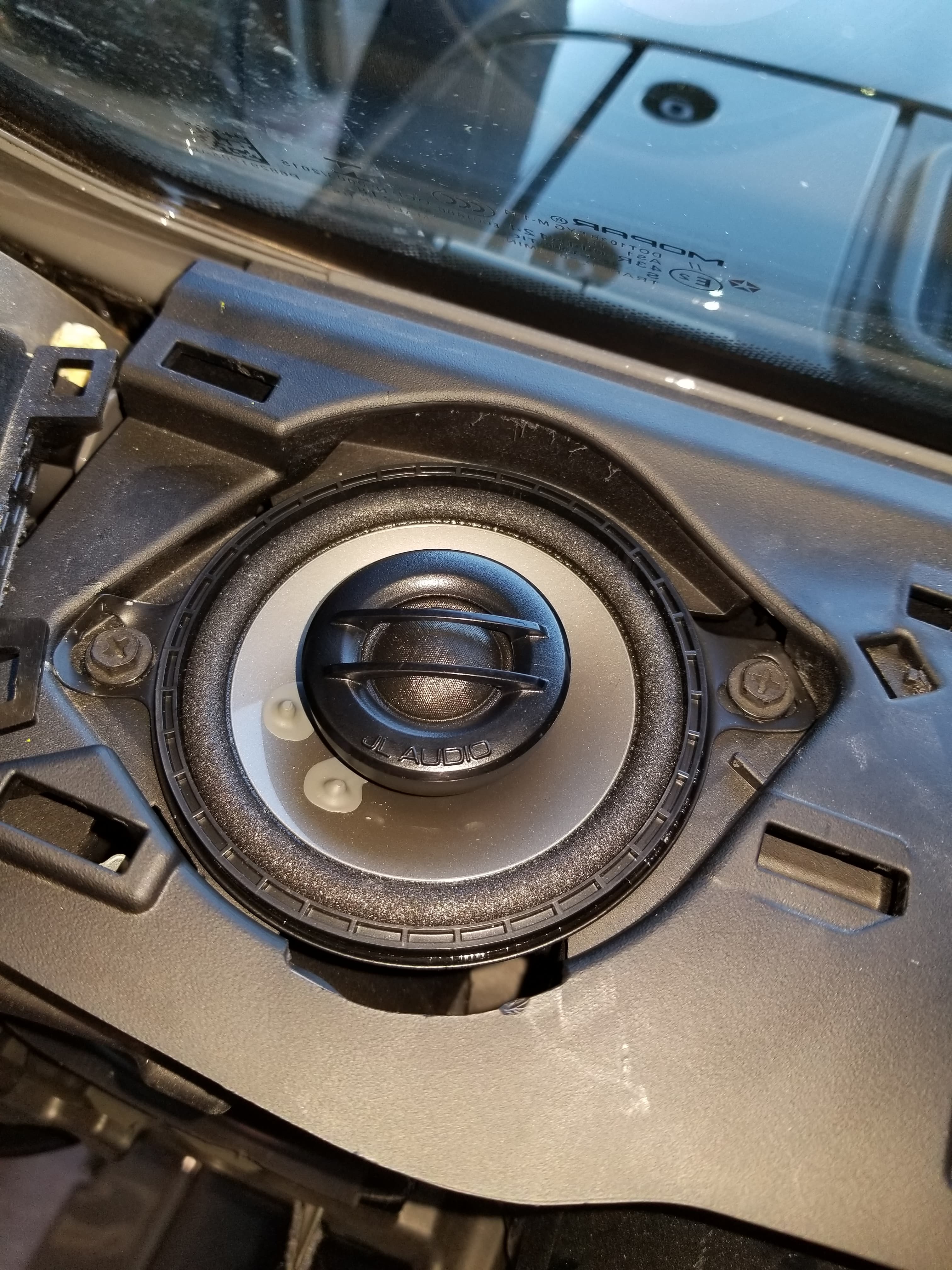 JL Audio speaker mounted in a black car dashboard housing near the front windshield glass.