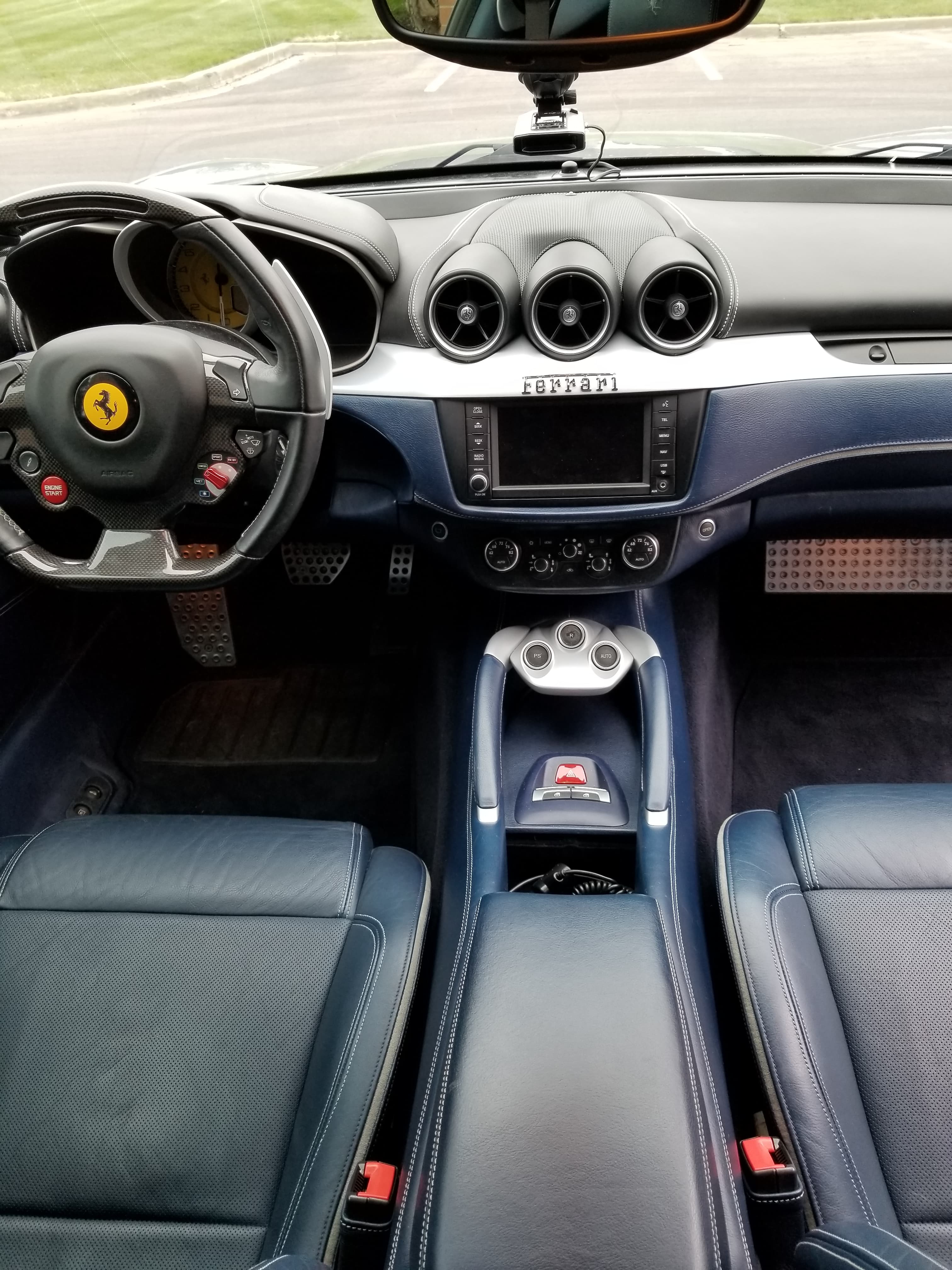 Luxurious blue leather interior of a Ferrari featuring a carbon fiber steering wheel and dashboard.