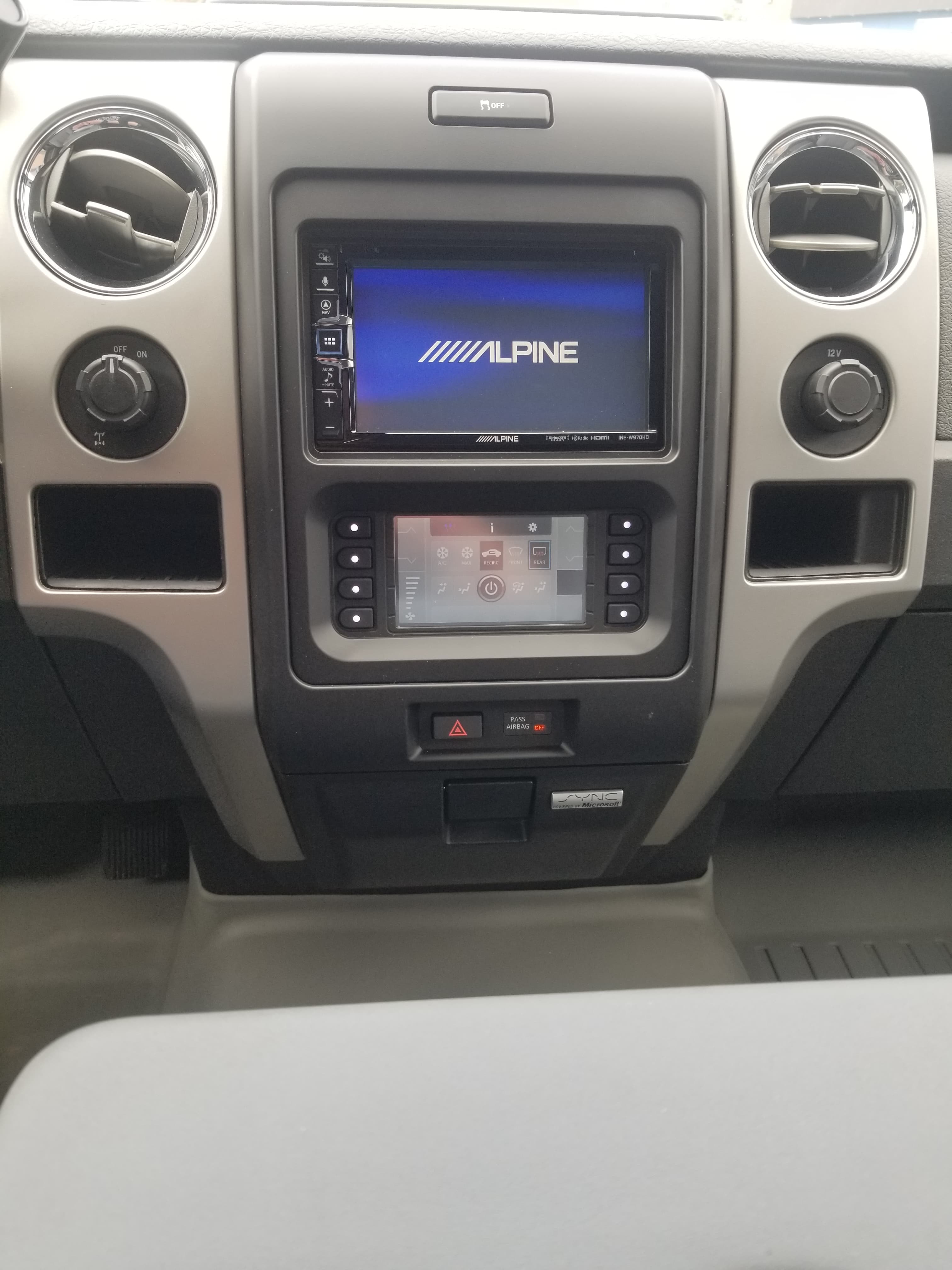 Vehicle dashboard featuring an Alpine infotainment screen, digital climate controls, and circular air vents.