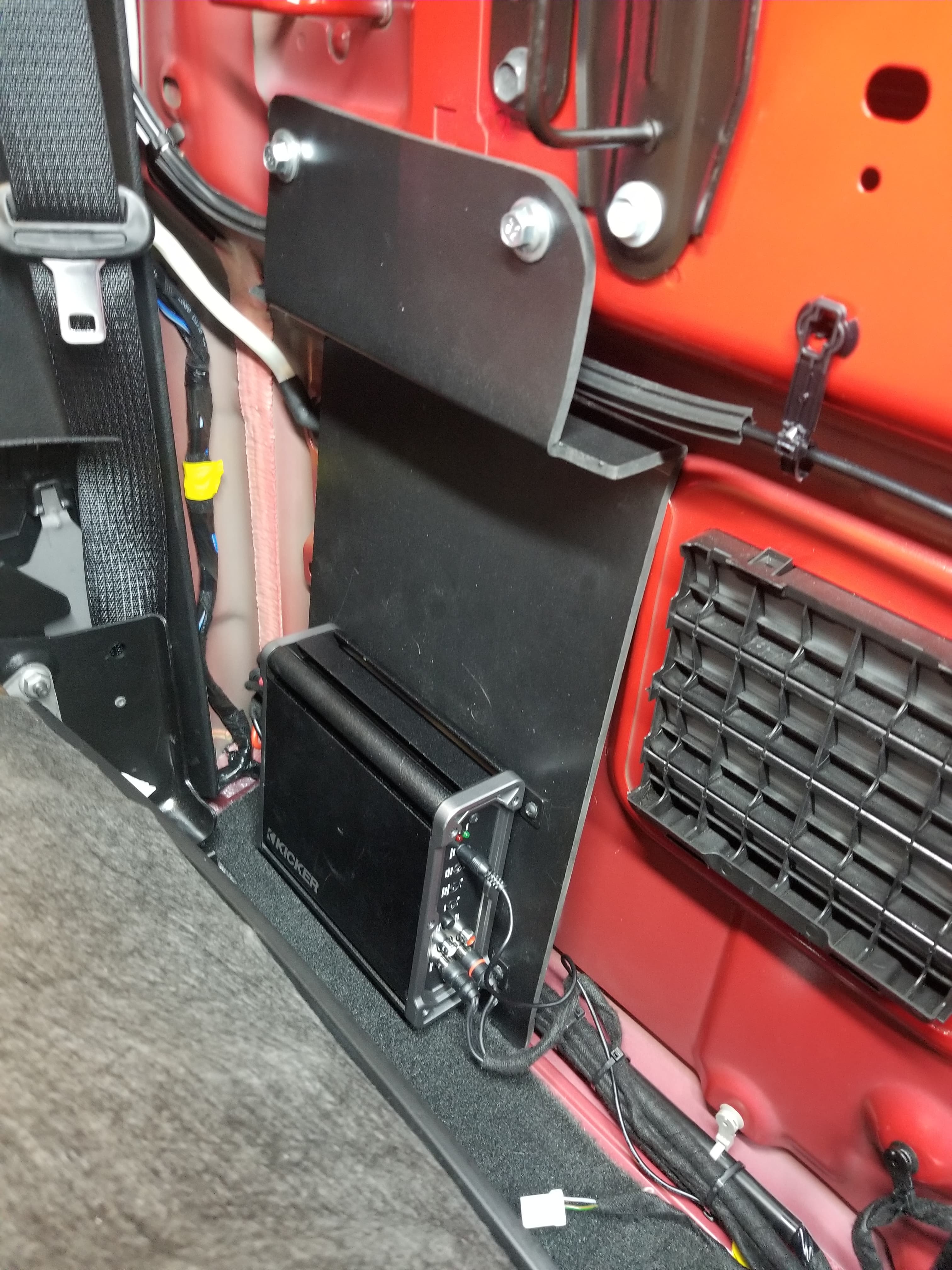 Black Kicker amplifier mounted on a custom metal bracket inside a red vehicle's cab.