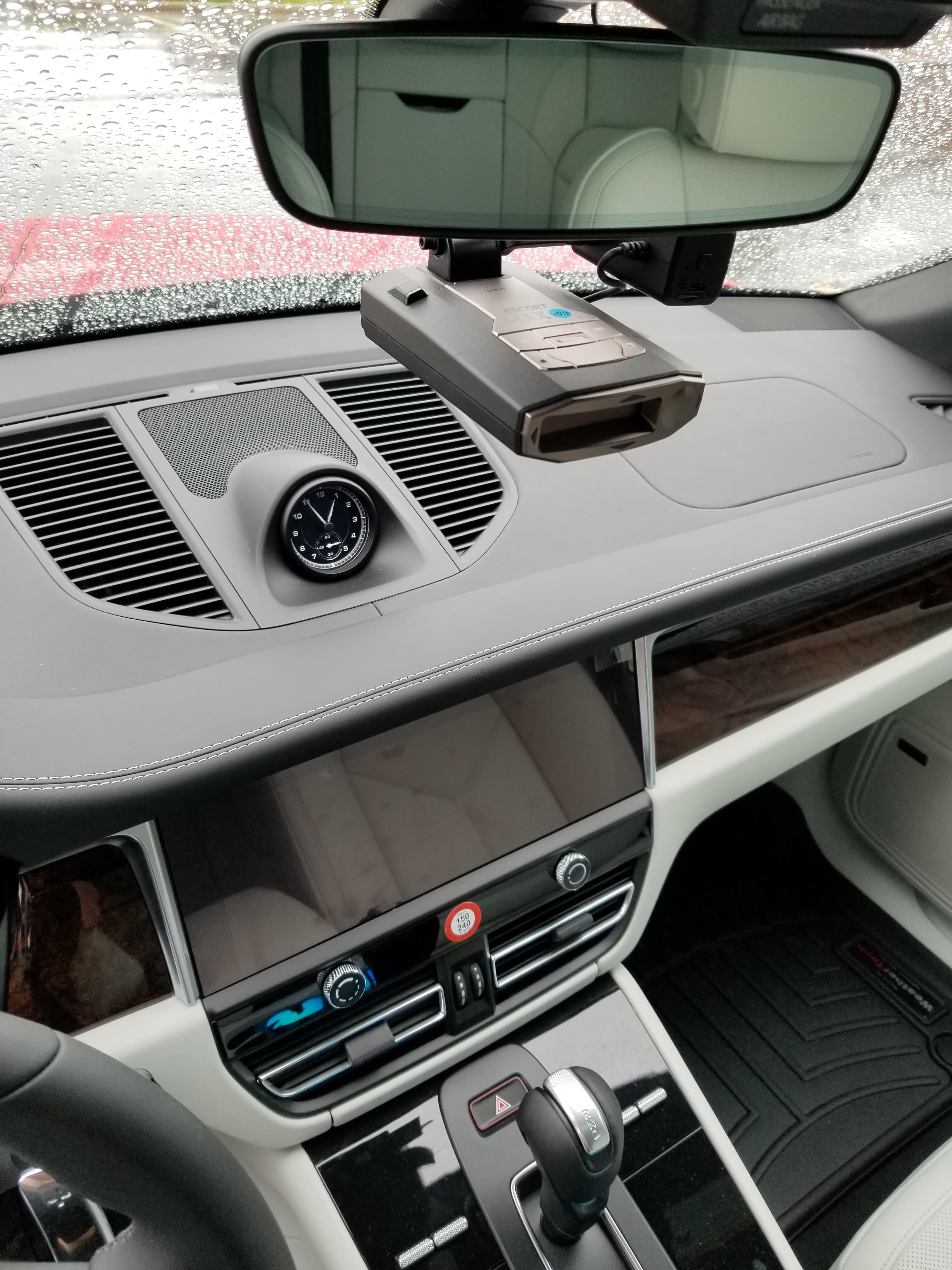 Grey leather car dashboard showing an analog clock, infotainment screen, and mounted radar detector.