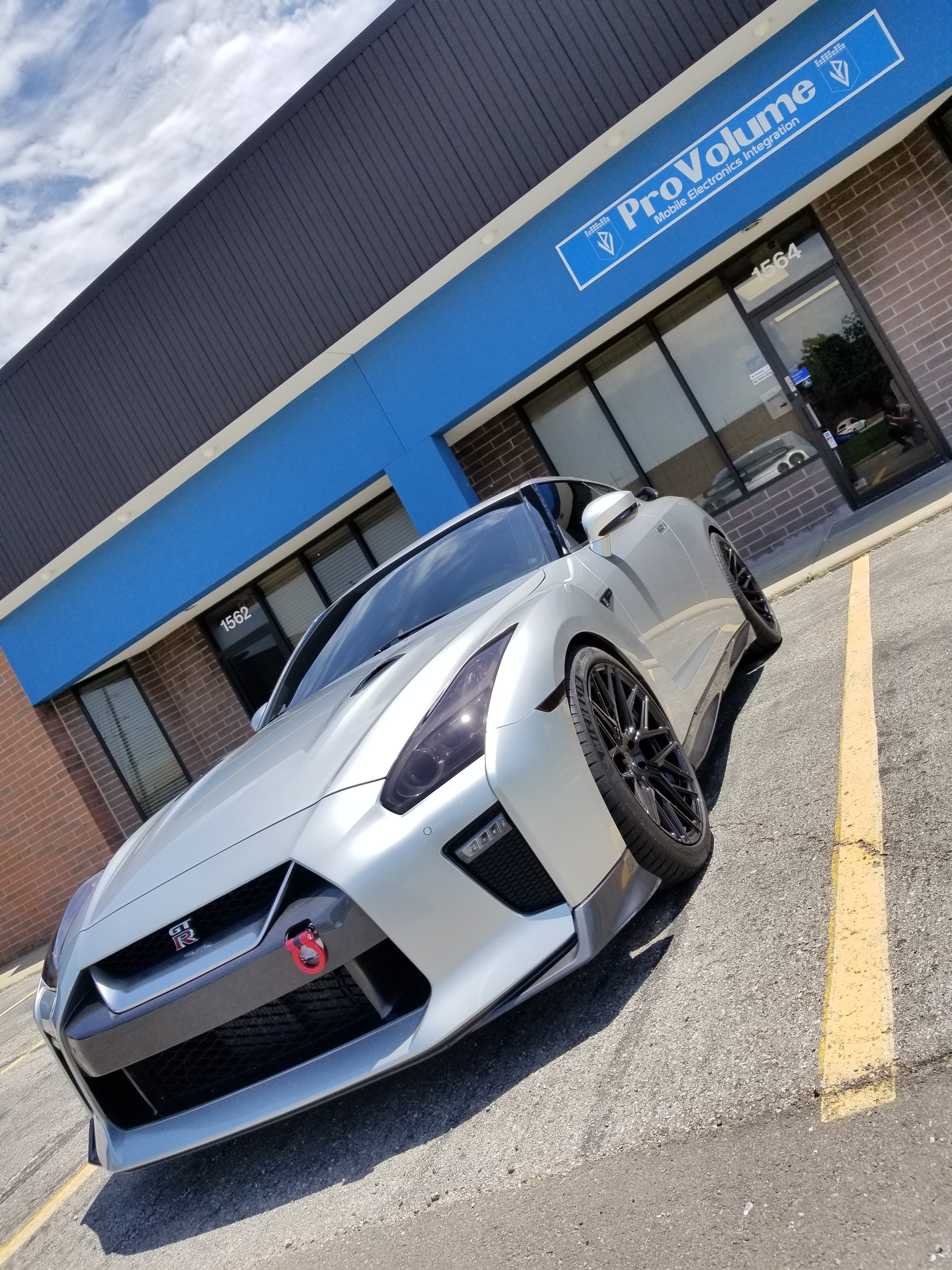 Silver Nissan GT-R with black wheels parked in front of a blue ProVolume storefront.