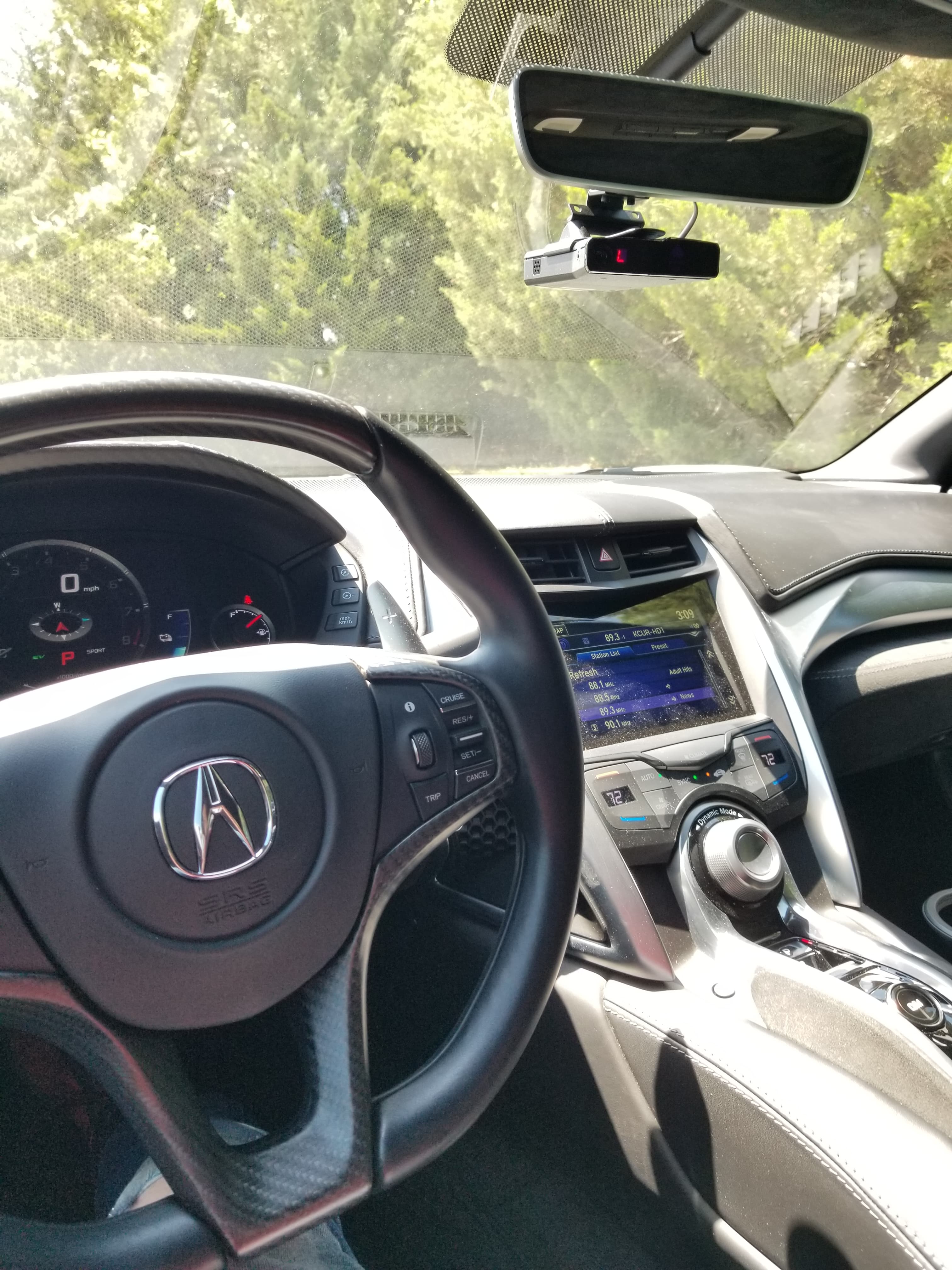 Driver's perspective inside an Acura, showing the steering wheel, dashboard, and infotainment screen.