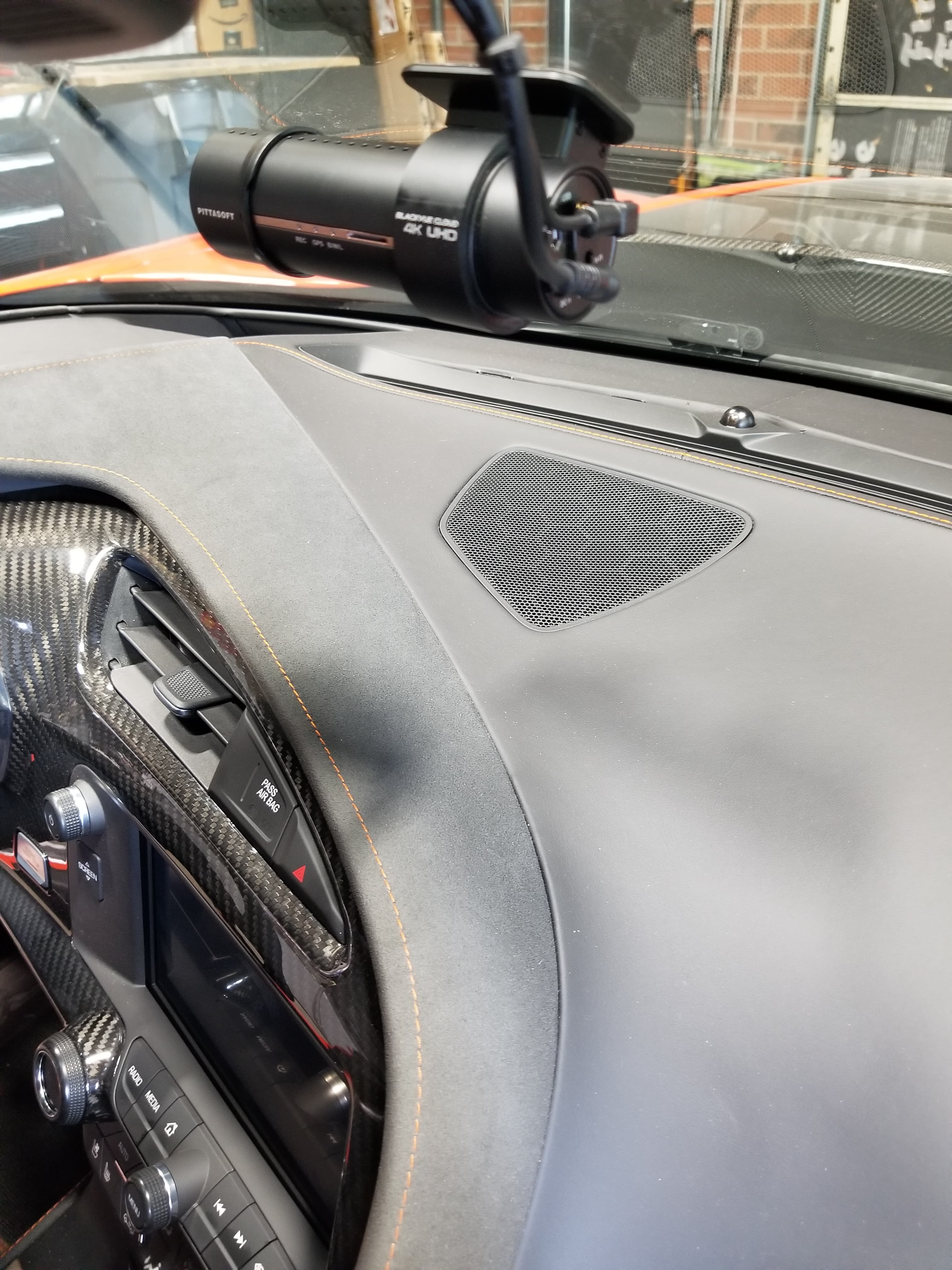 BlackVue dashcam mounted on a windshield above a car dashboard with orange stitching and carbon fiber.