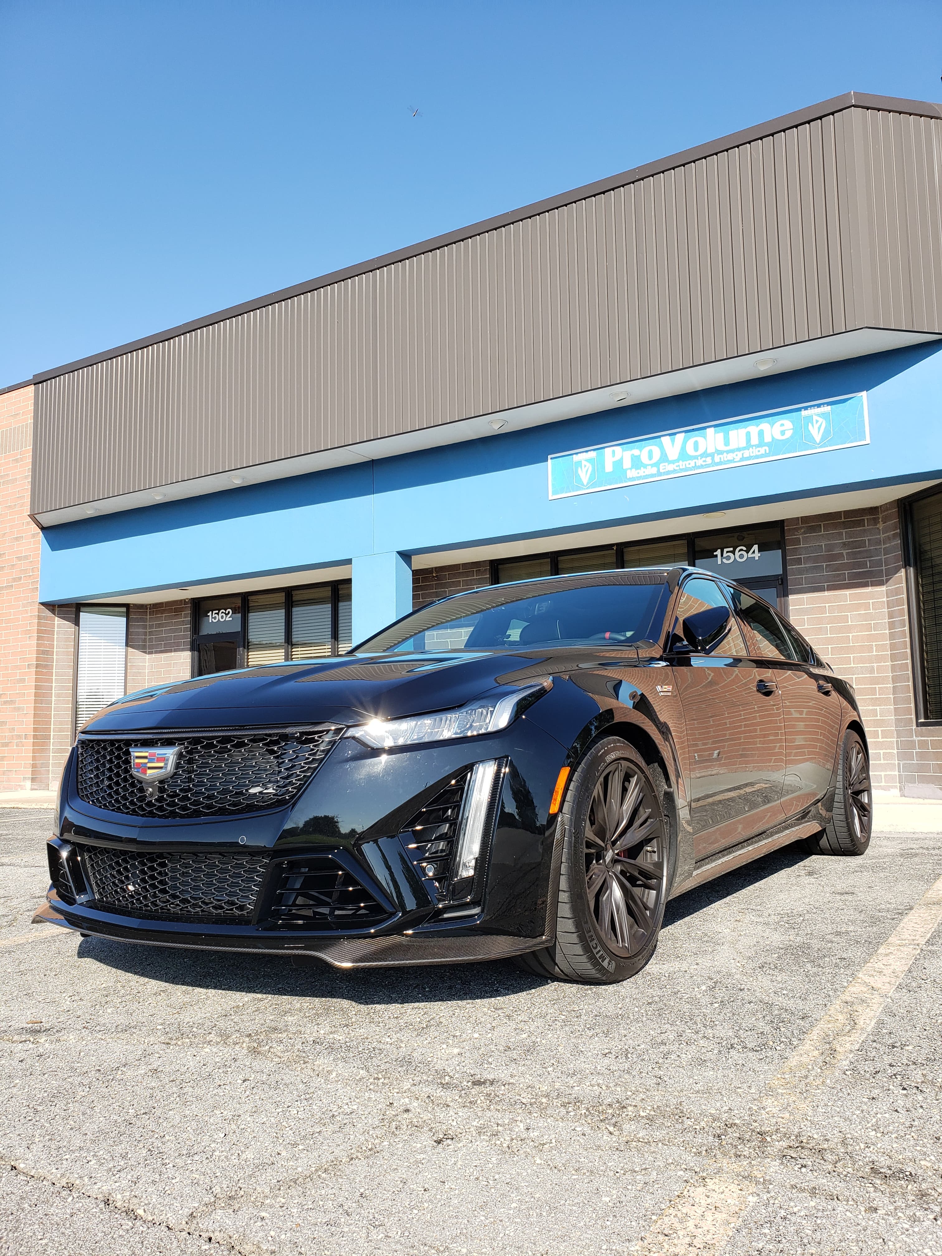 Black Cadillac CT5-V Blackwing parked in front of a ProVolume electronics store building.