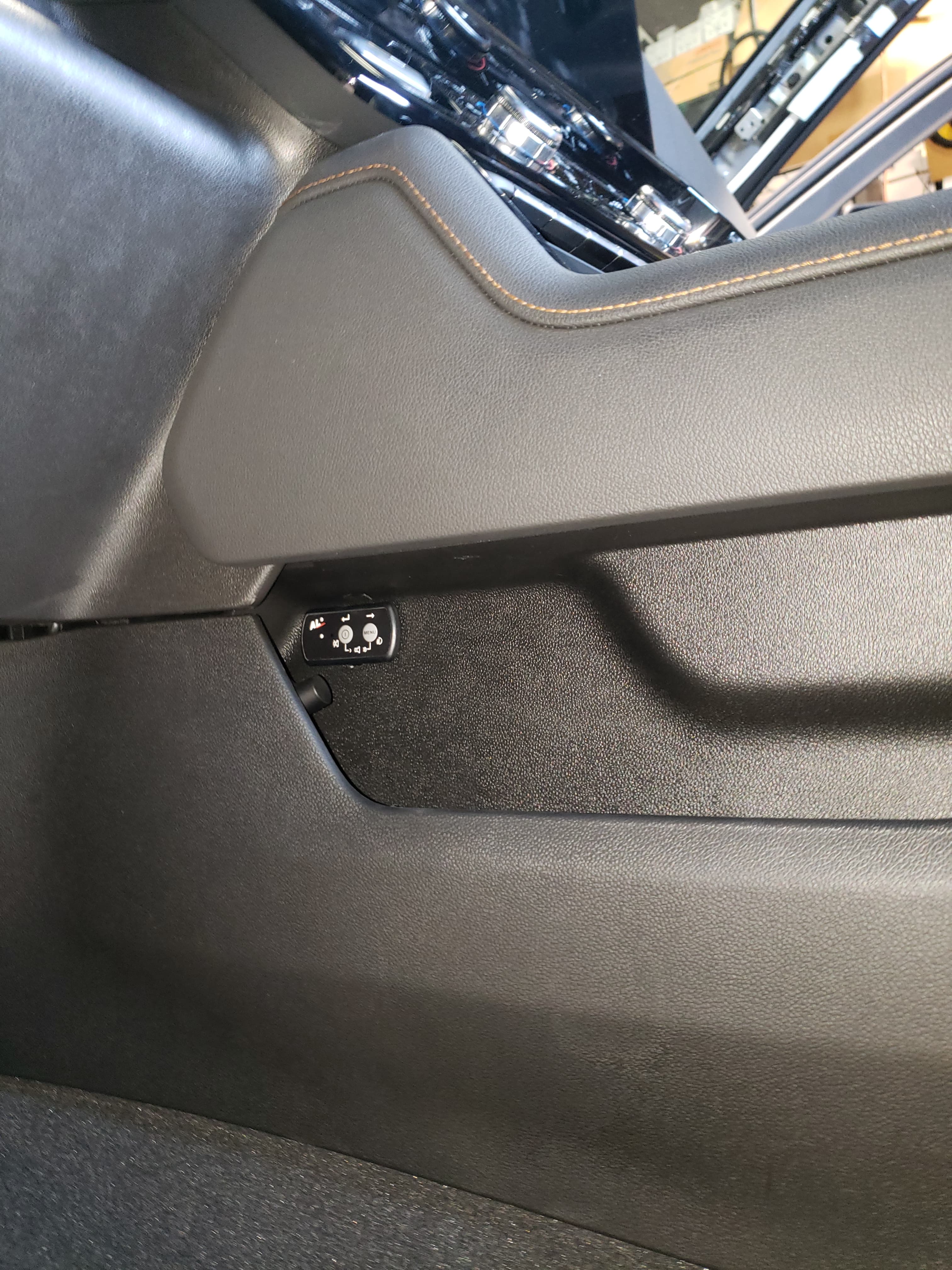 Black leather car seat with orange stitching and side-mounted electronic seat adjustment controls.