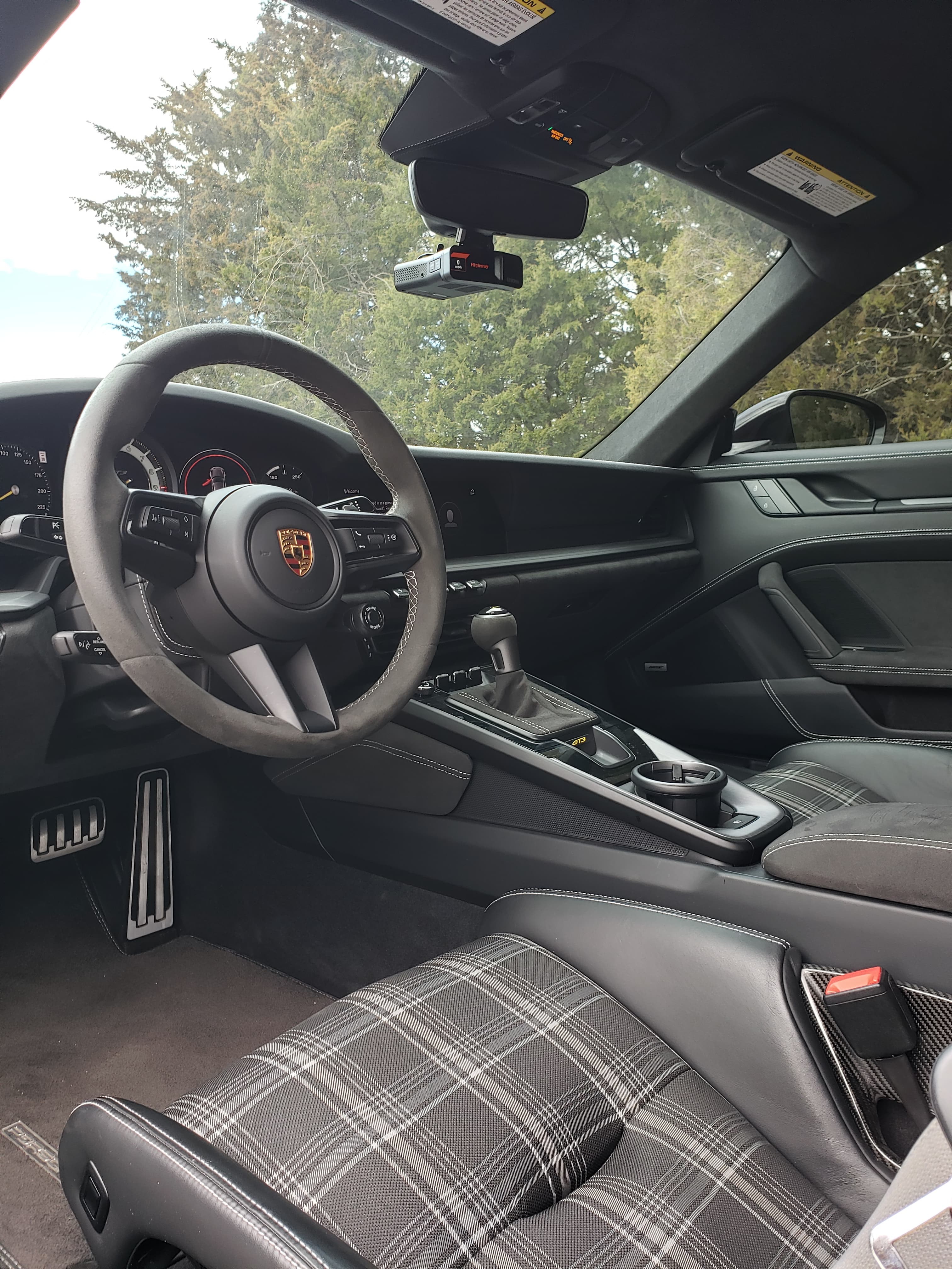 Modern Porsche interior featuring a suede steering wheel, manual transmission, and plaid patterned seats.