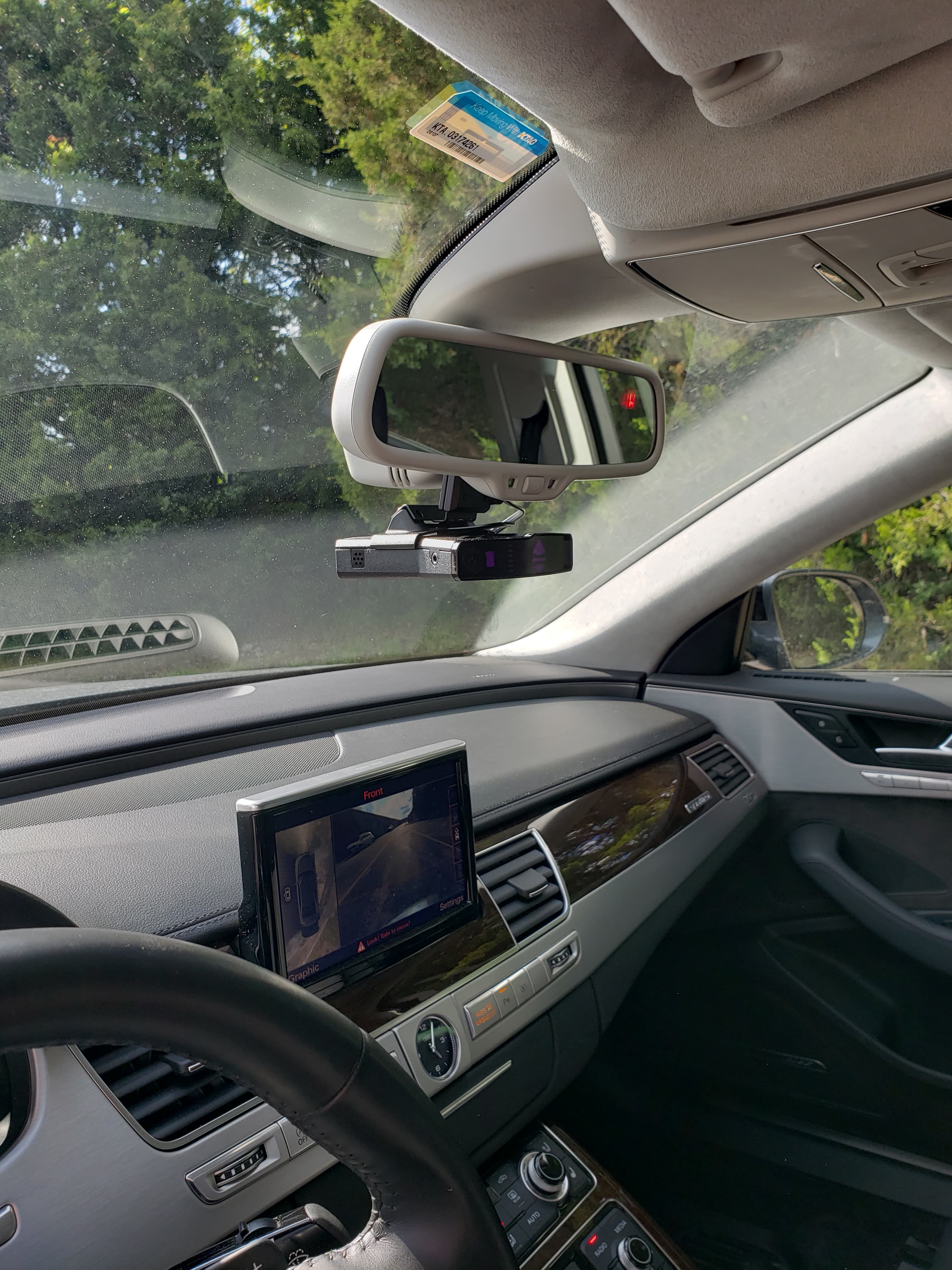 Car interior featuring a radar detector on the rearview mirror and a dashboard camera display.