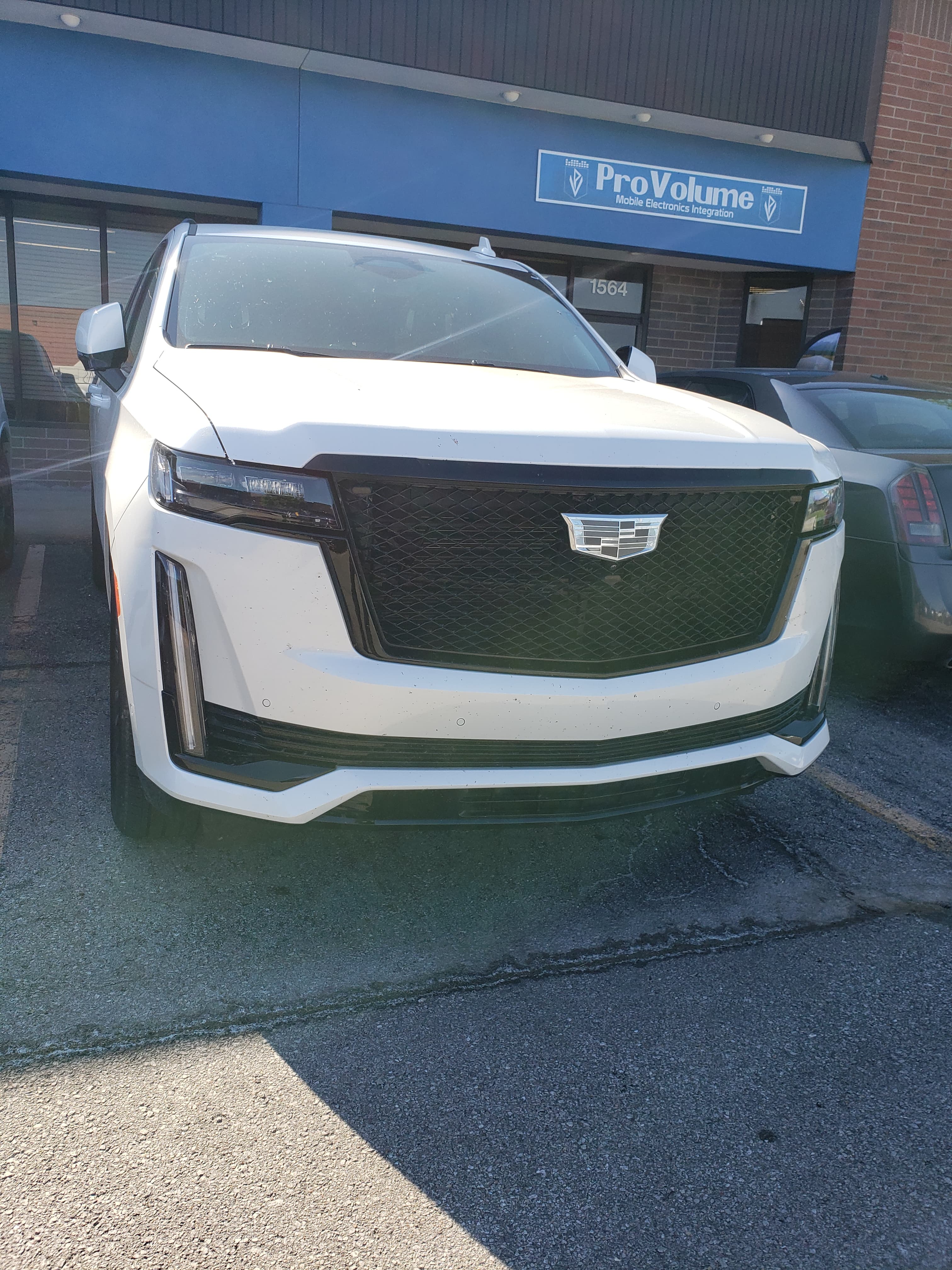 White Cadillac SUV with a black grille parked outside a ProVolume mobile electronics shop.
