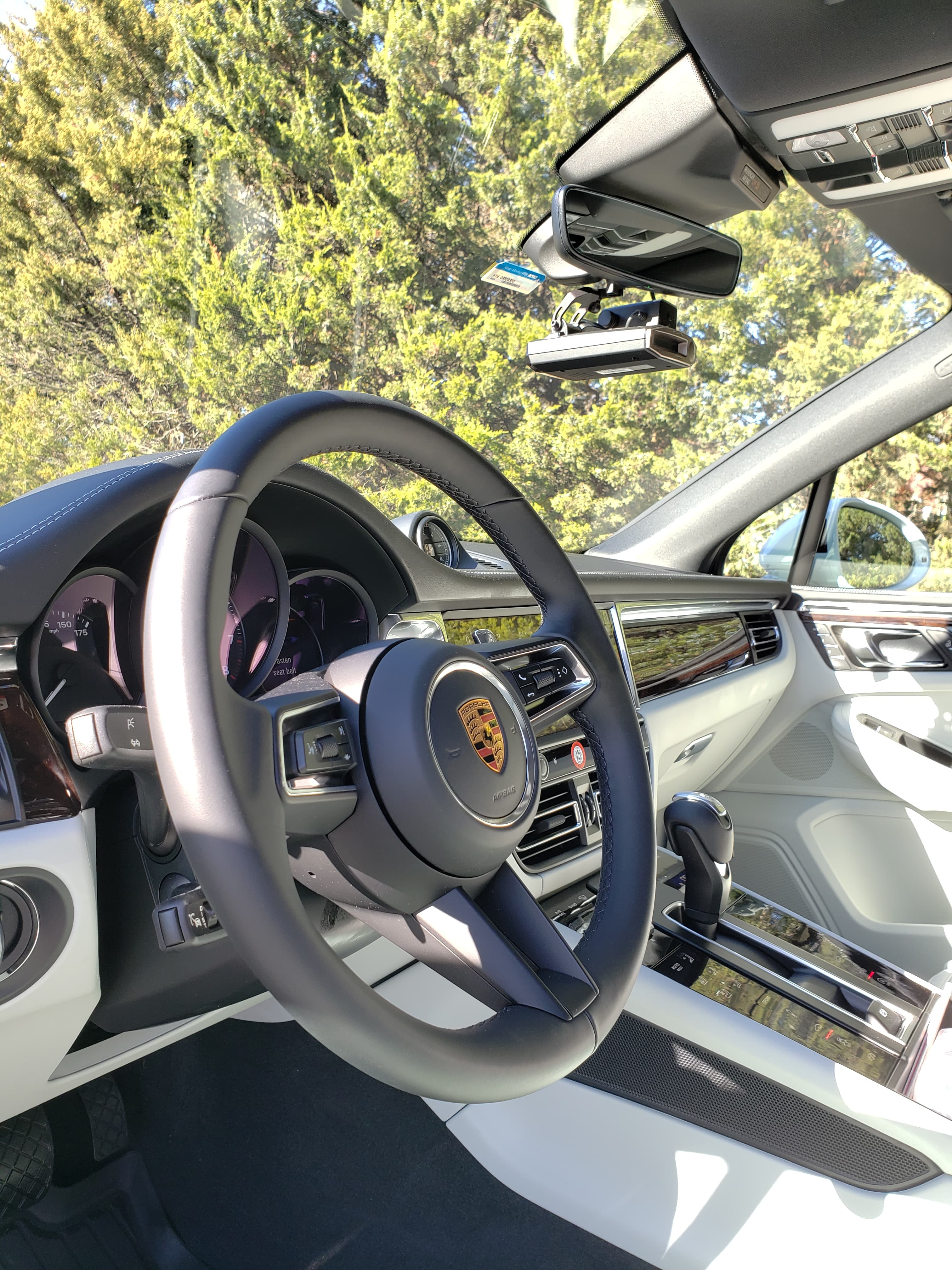 Sunlit Porsche interior showing a black steering wheel, white dashboard, and a mounted dashcam.