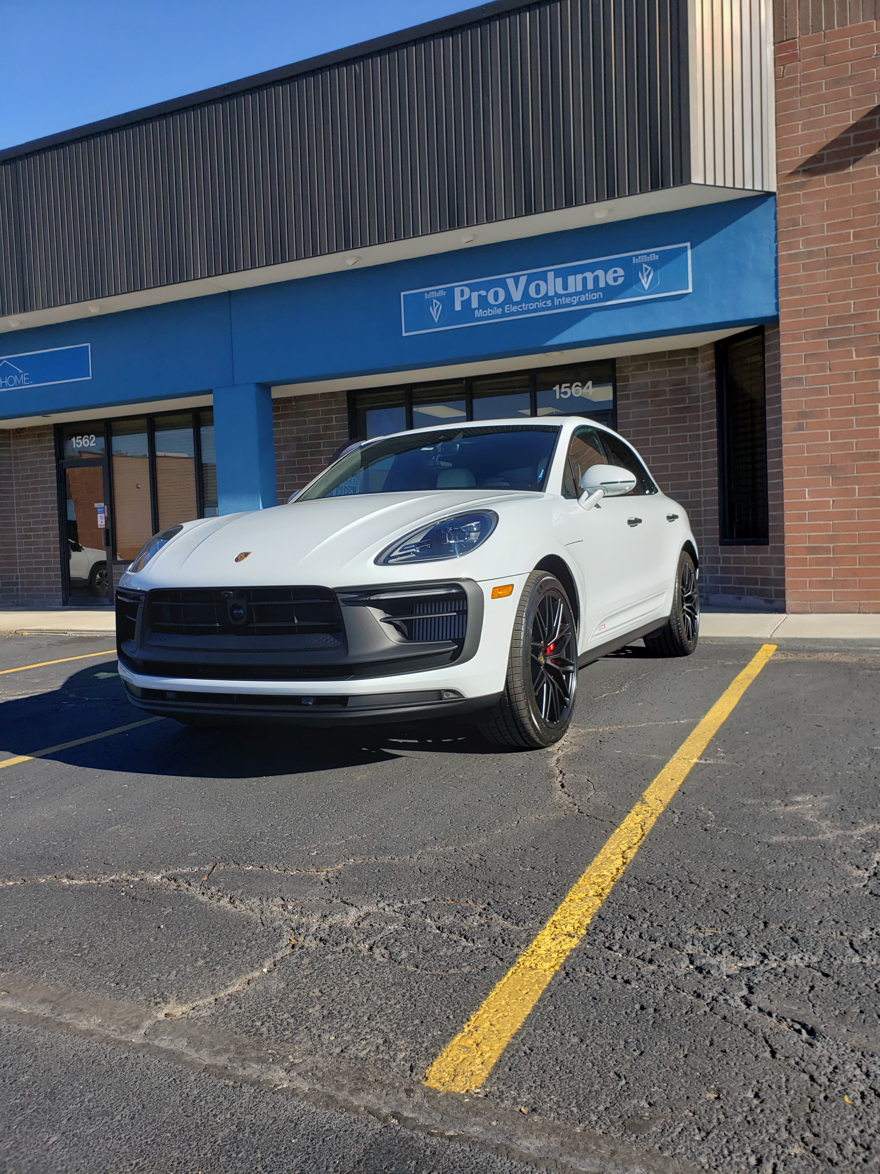 A white Porsche Macan GTS parked in front of a ProVolume mobile electronics storefront.