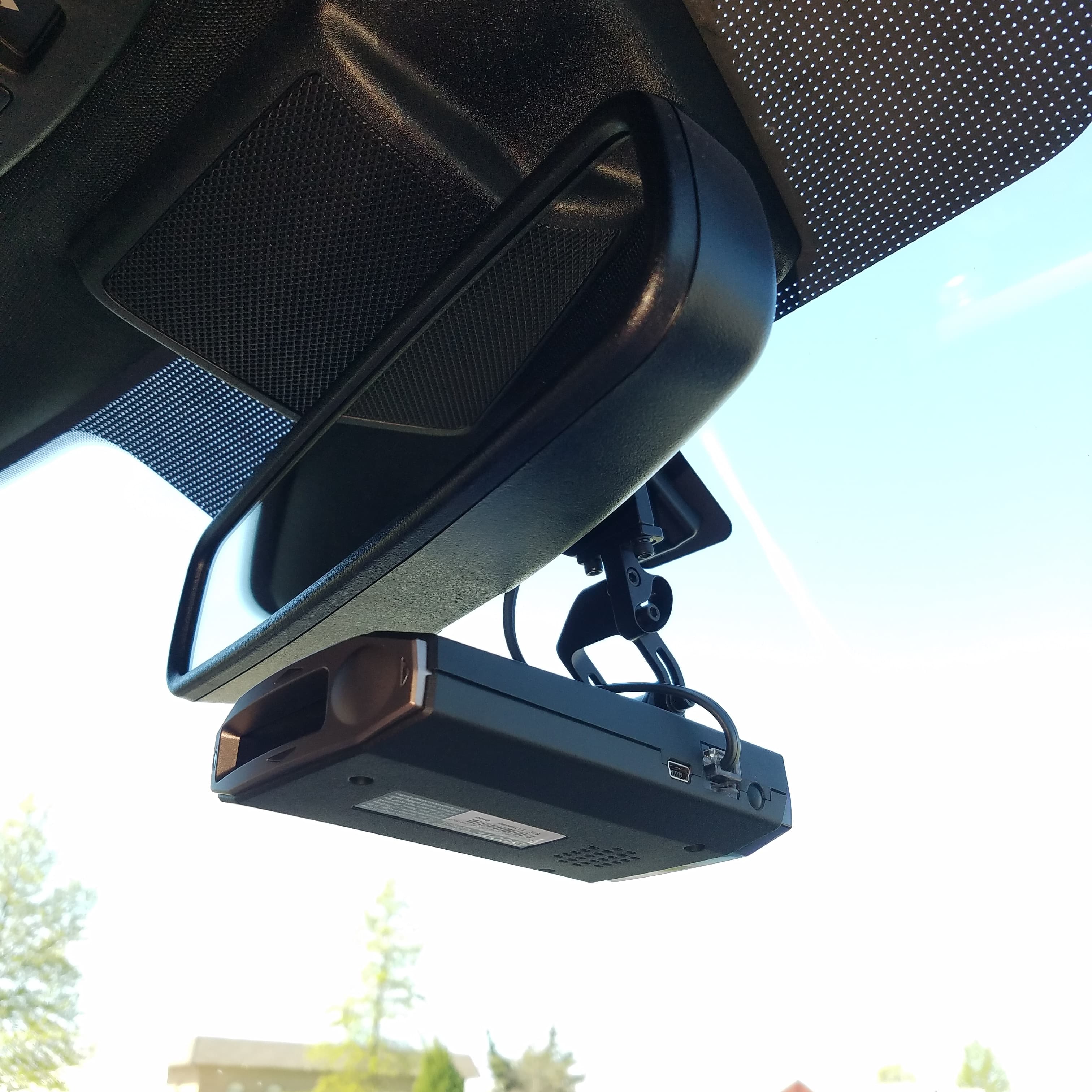 A black radar detector mounted to the stem of a car's rearview mirror.