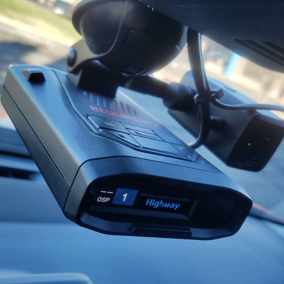 Black radar detector mounted on a car windshield, featuring a digital display showing "OSP 1 Highway".