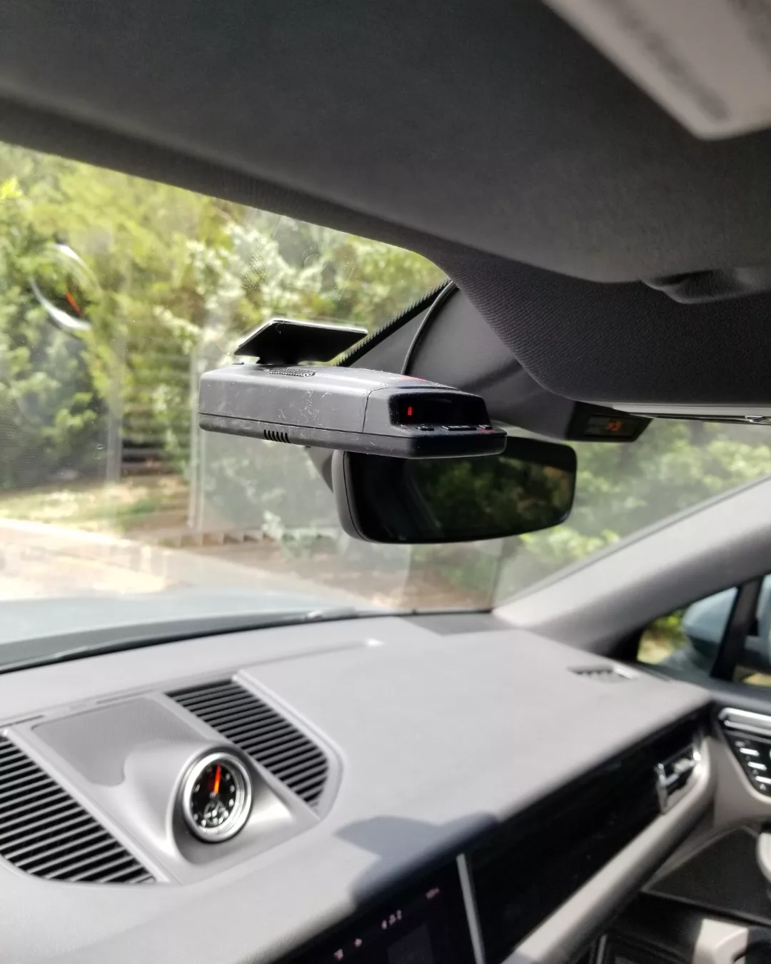 Black radar detector mounted on a car windshield above the rearview mirror and dashboard.