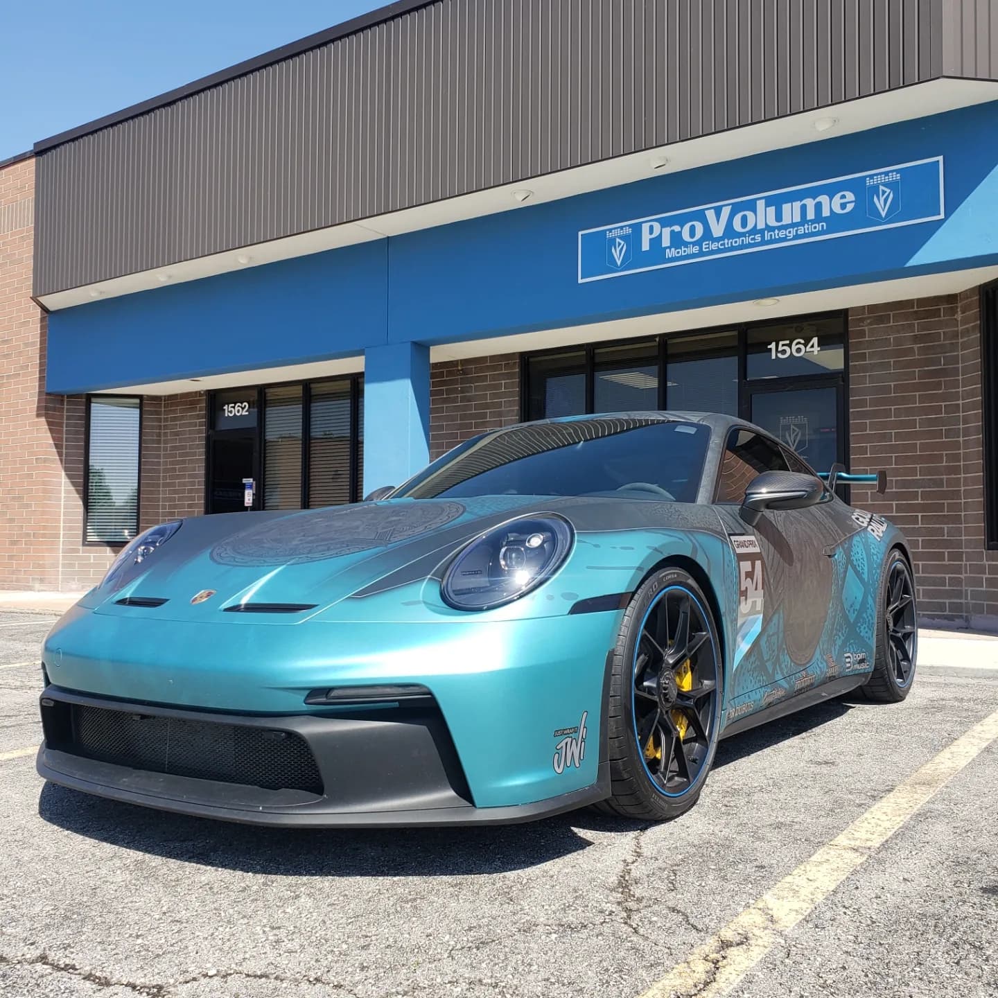 Teal and grey custom-wrapped Porsche 911 GT3 parked outside a ProVolume electronics store.