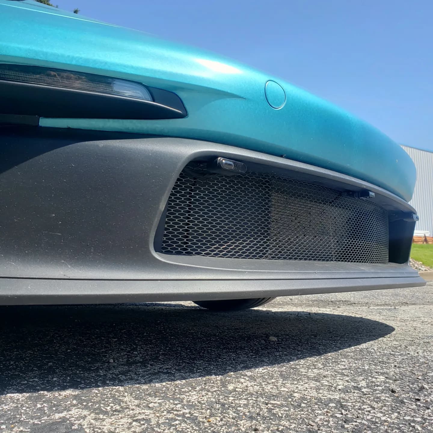 Low angle view of a teal car's front bumper with black mesh grille and trim.