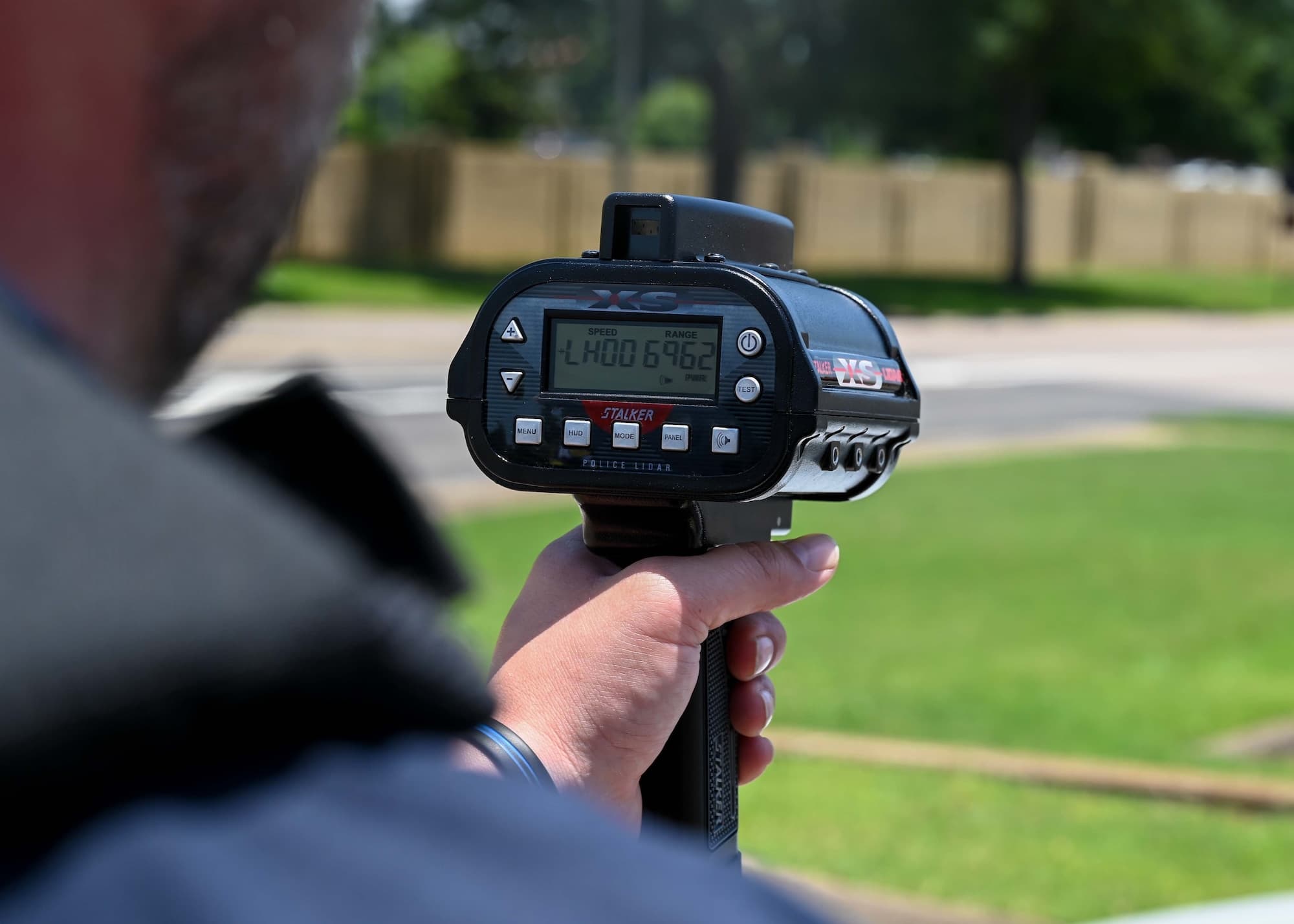 Handheld Stalker XS police lidar gun displaying speed and range data near a road.